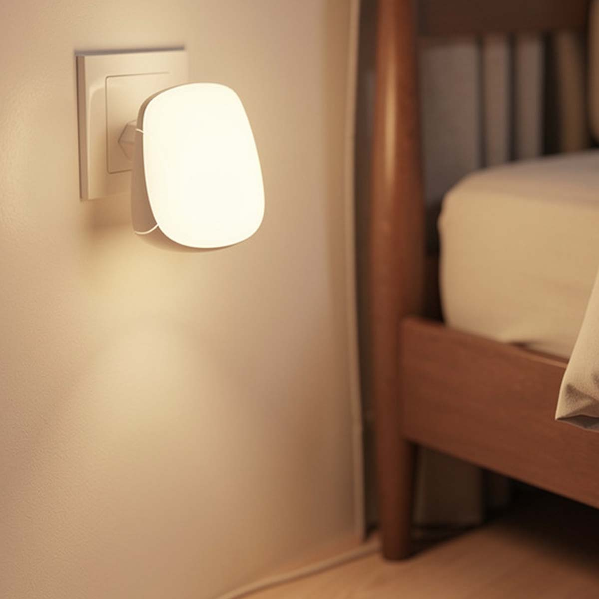 Un enchufe de luz nocturna blanco brilla junto a una cama de madera.