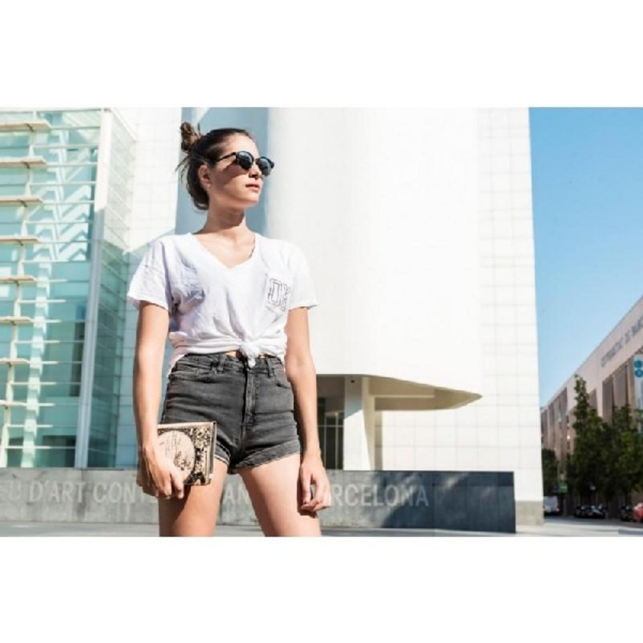 Una mujer con gafas de sol y moño delante de un edificio moderno.
