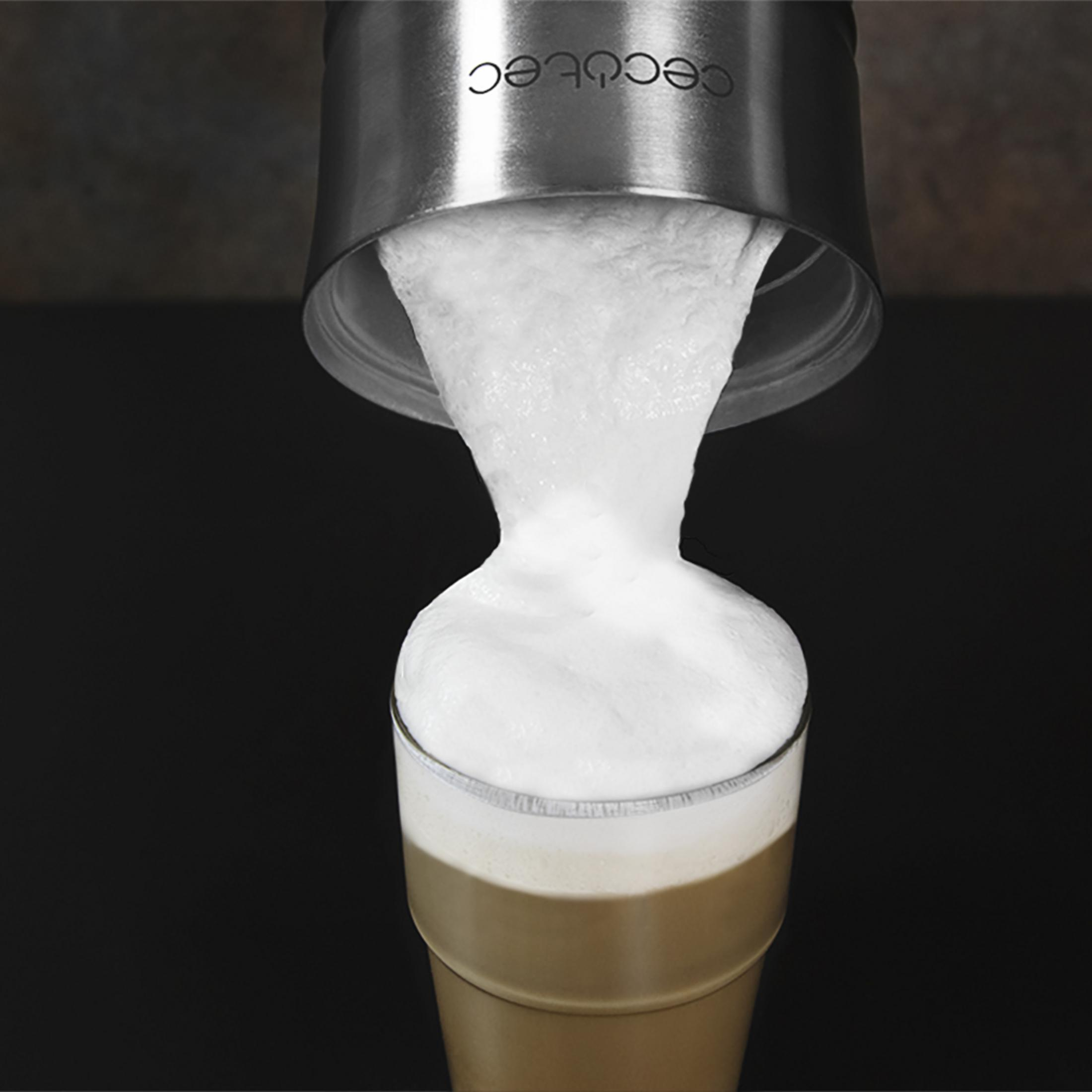 Schiuma di latte che scorre da un contenitore argentato in un bicchiere di caffè.