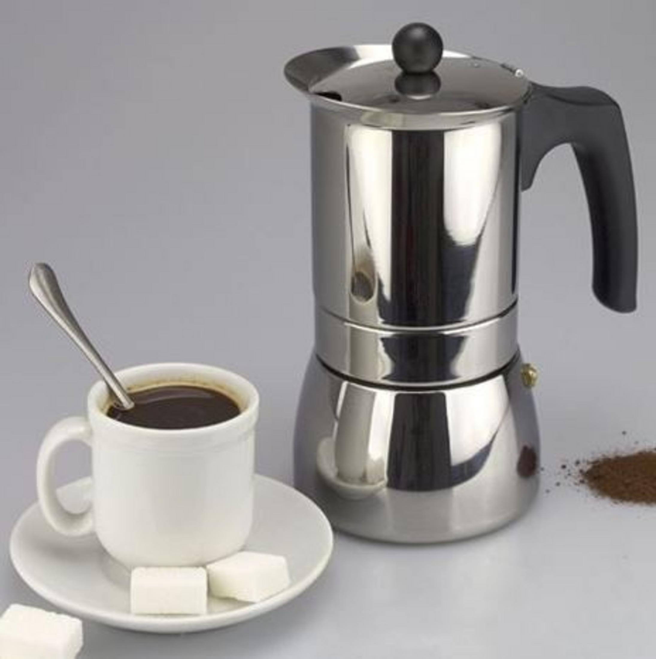Una cafetera italiana plateada junto a una taza de café blanca con cuchara y terrones de azúcar.