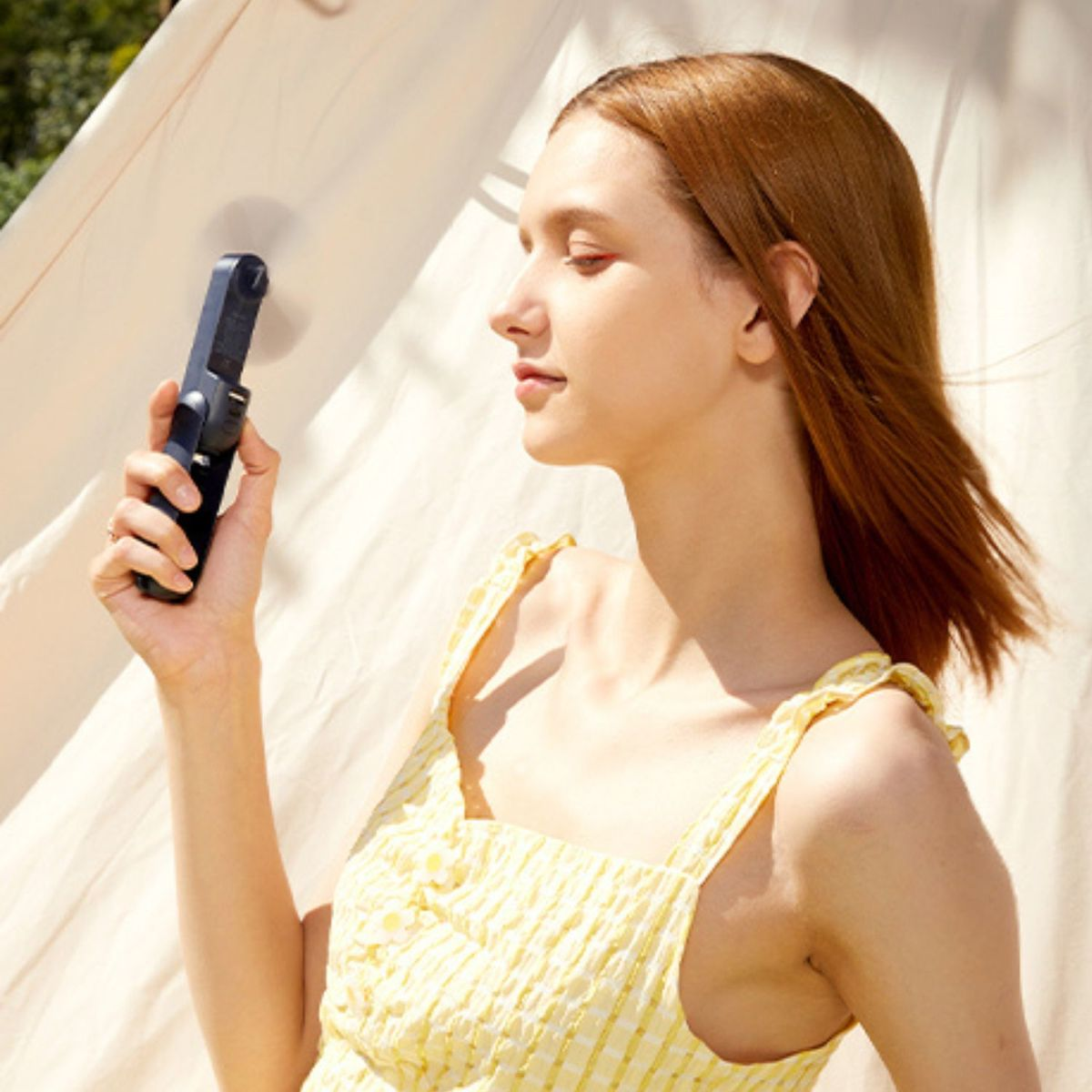 Eine Frau mit roten Haaren hält einen kleinen schwarzen Ventilator in der Hand.