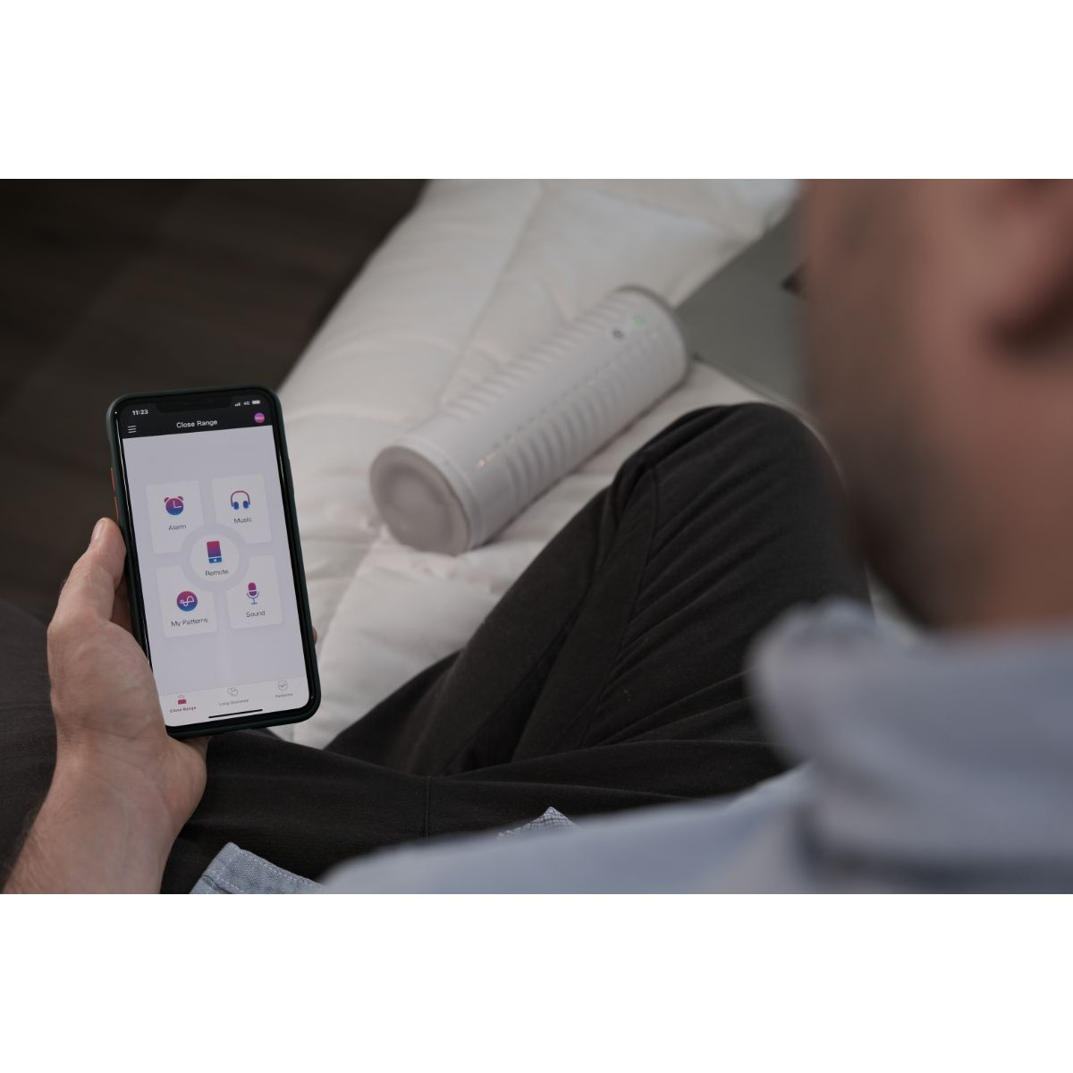 Osoba trzyma smartfon z aplikacją, obok leży białe urządzenie.