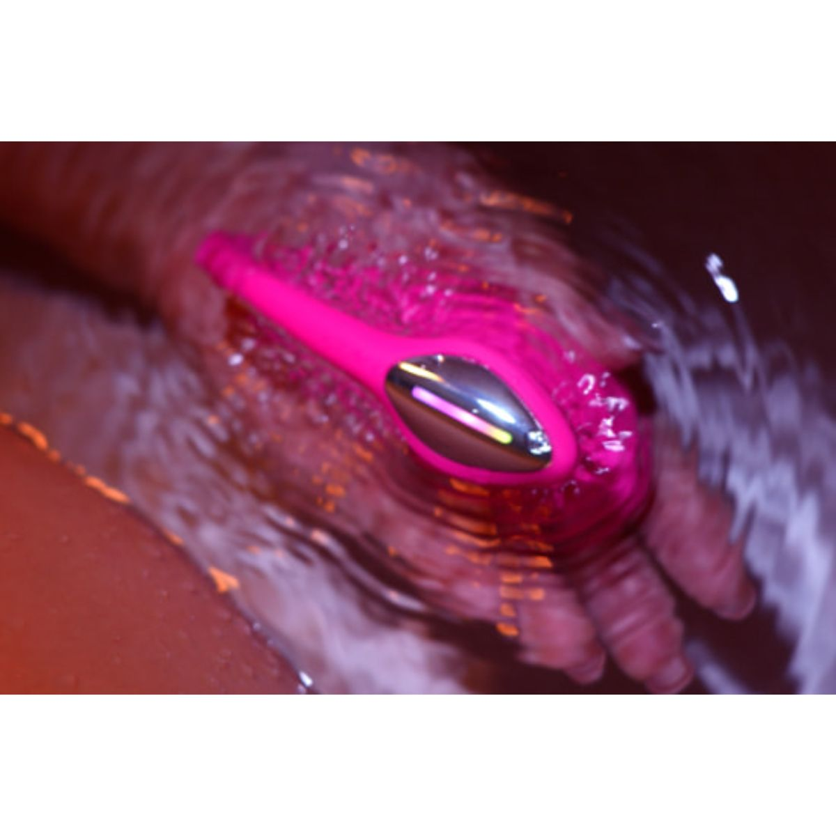 Eine Hand hält einen pinken Vibrator unter Wasser. Reflektionen sind sichtbar.