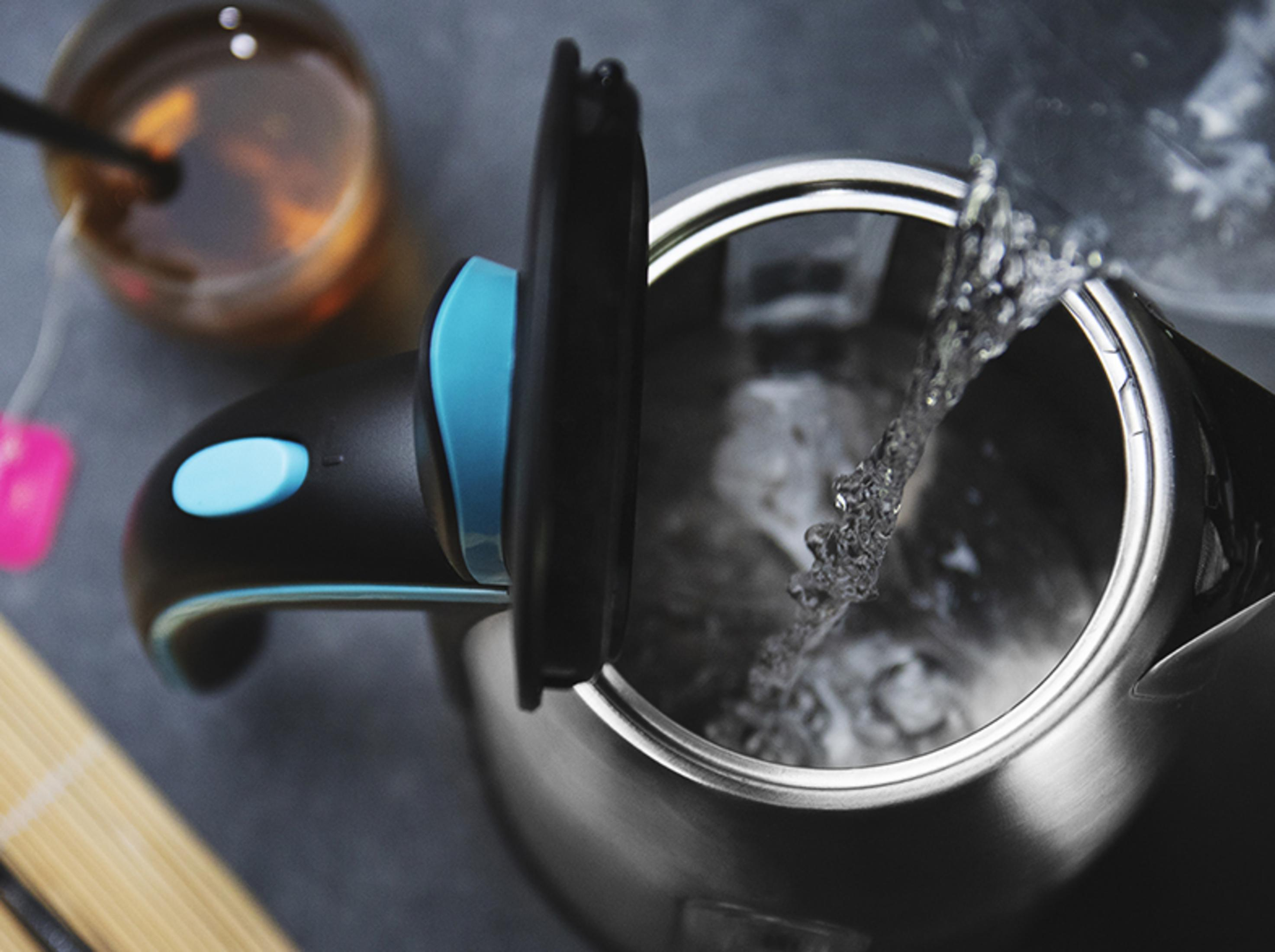 L'acqua scorre in un bollitore aperto accanto a una tazza di tè.