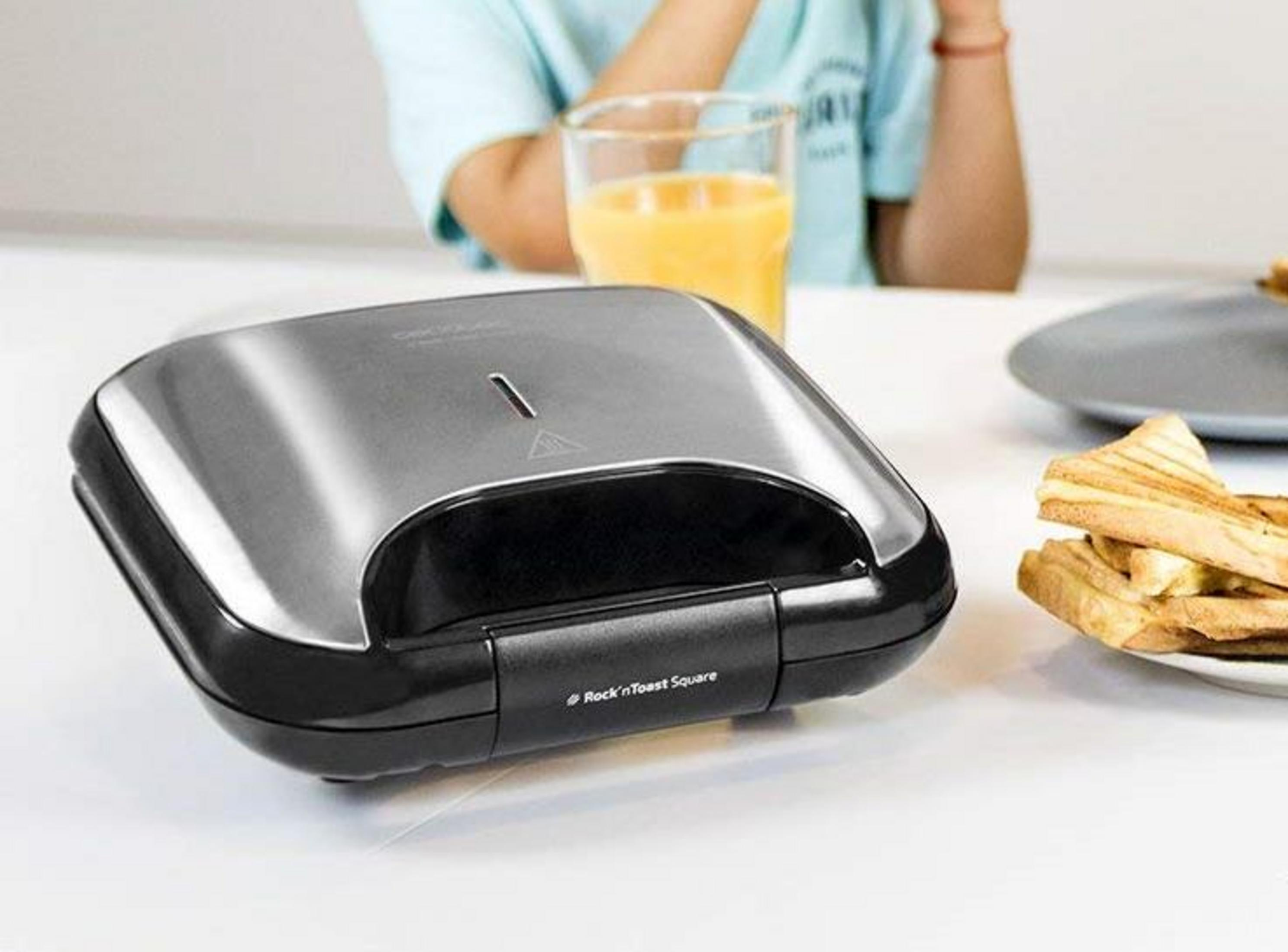 Un sandwich maker chiuso con toast su un piatto e un bicchiere di succo nelle vicinanze.
