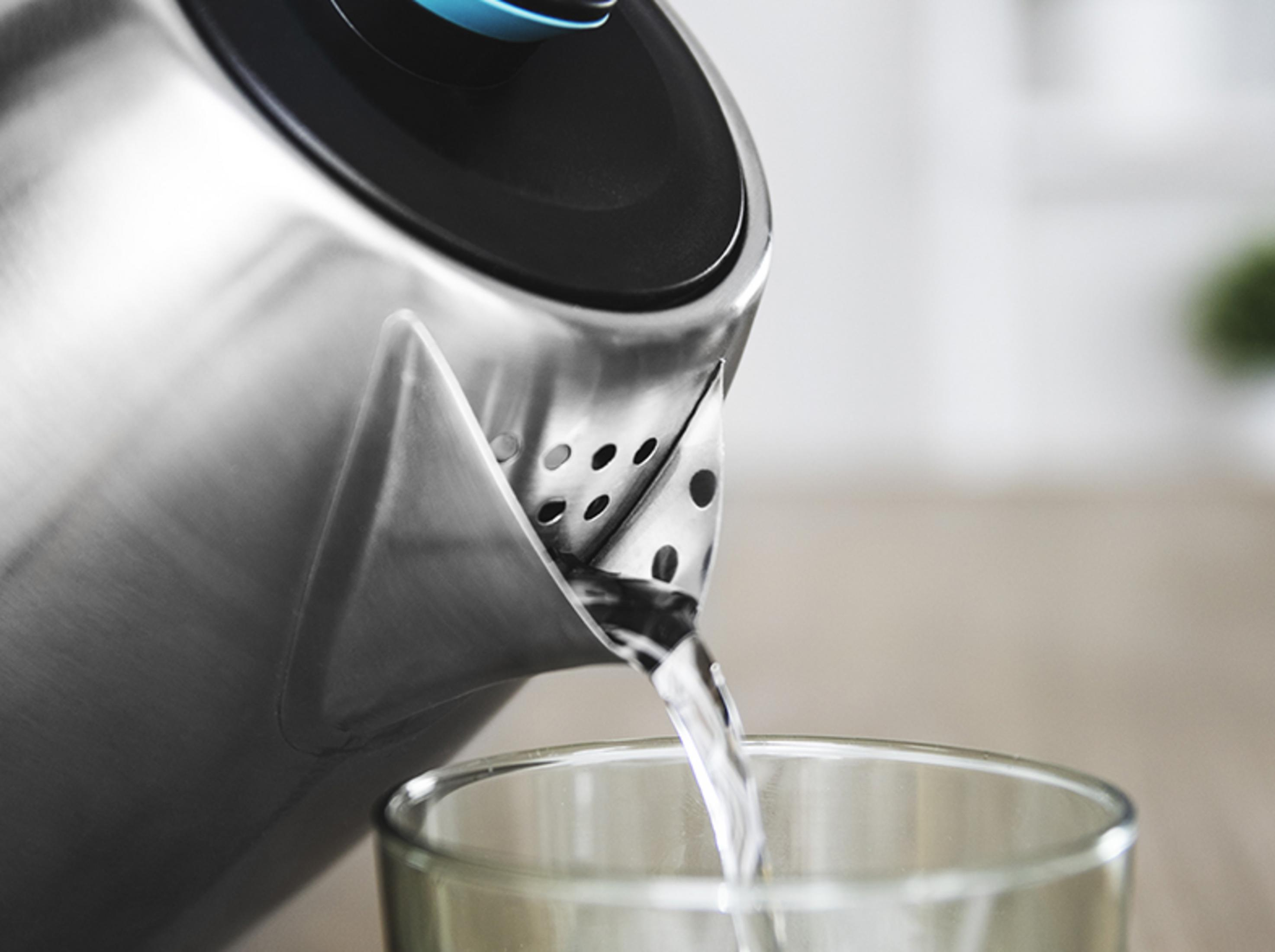Acqua che cola da un bollitore d'argento in un bicchiere.