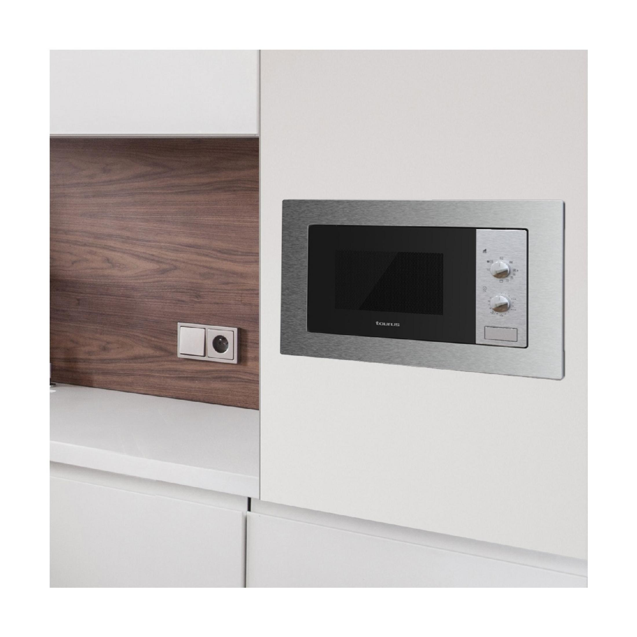 Microondas empotrado Taurus con marco plateado en pared blanca.