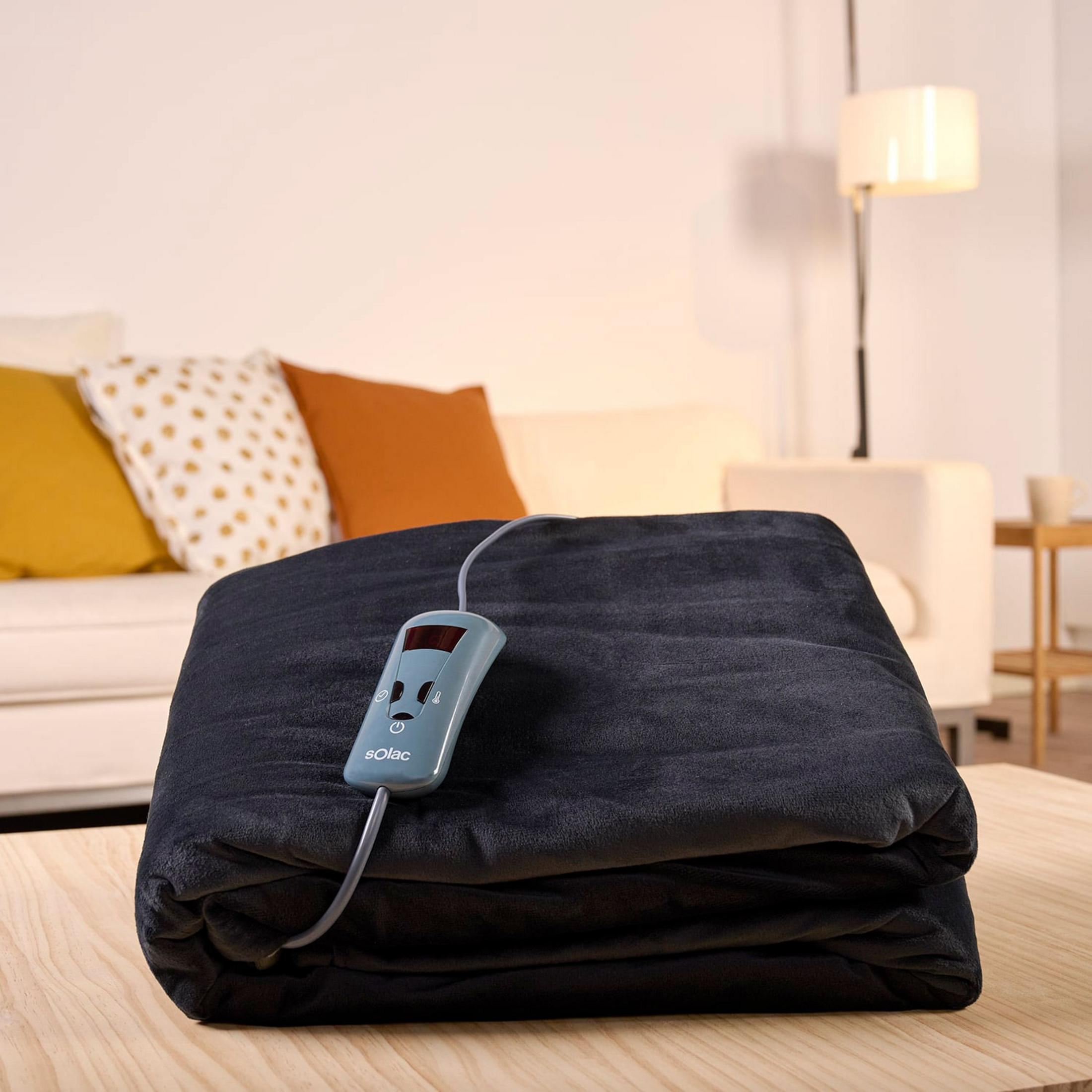 Una coperta elettrica in peluche scuro e piegata con controller blu poggia su tavolo legno.