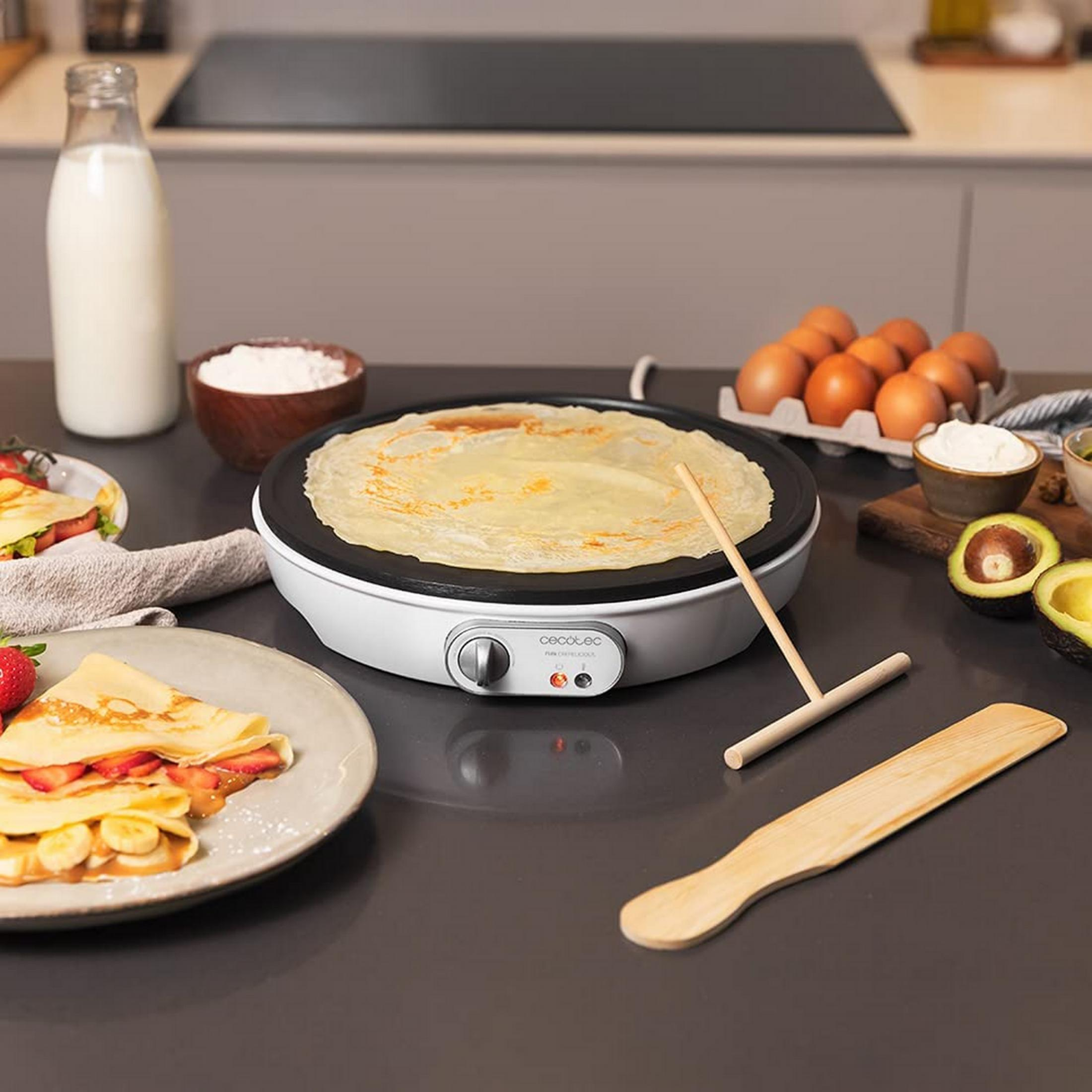 Crepes vengono preparate su una piastra elettrica bianca con bacche e banane.