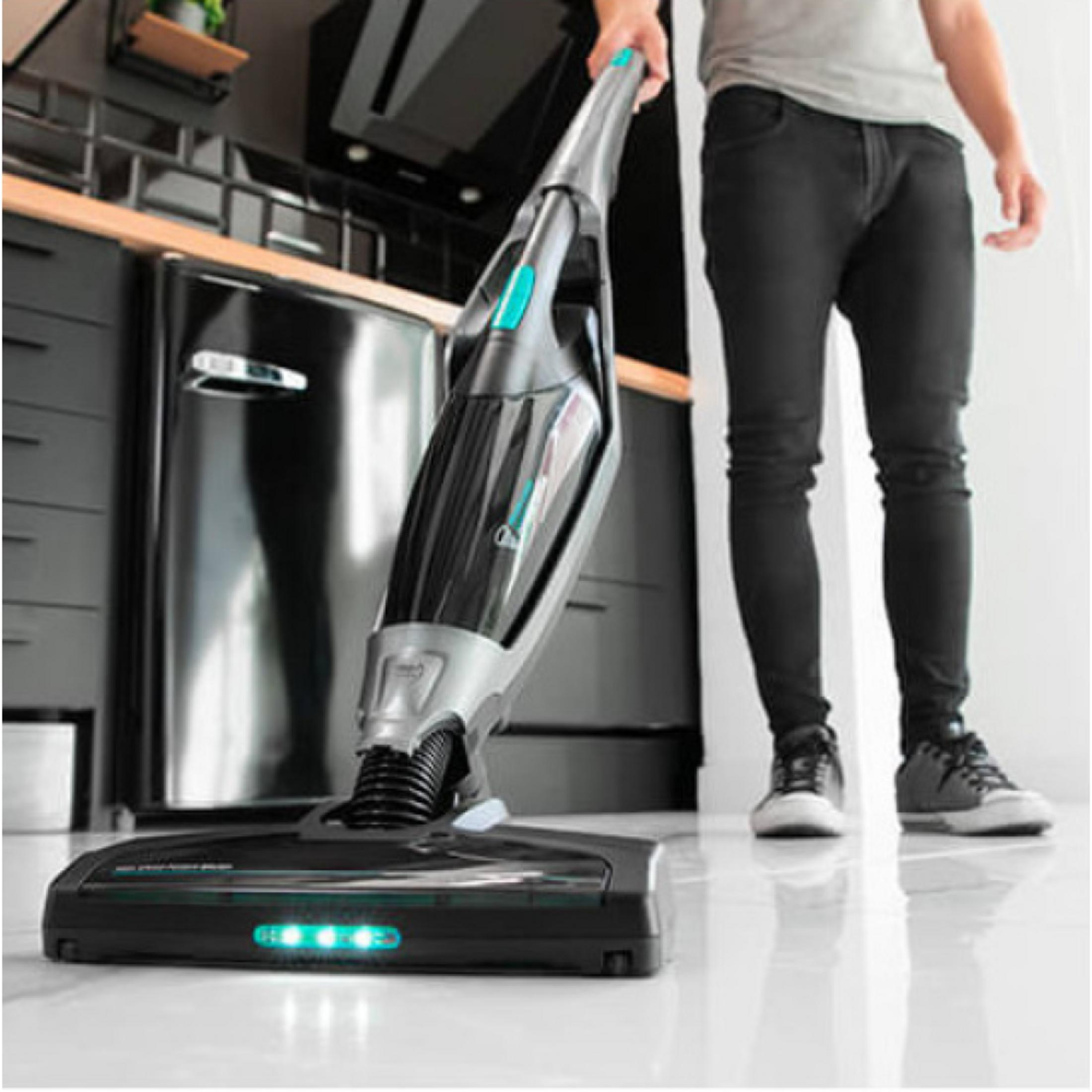 Ein Mann hält einen kabellosen Staubsauger in einer Küche mit schwarzen Schränken und Kühlschrank.