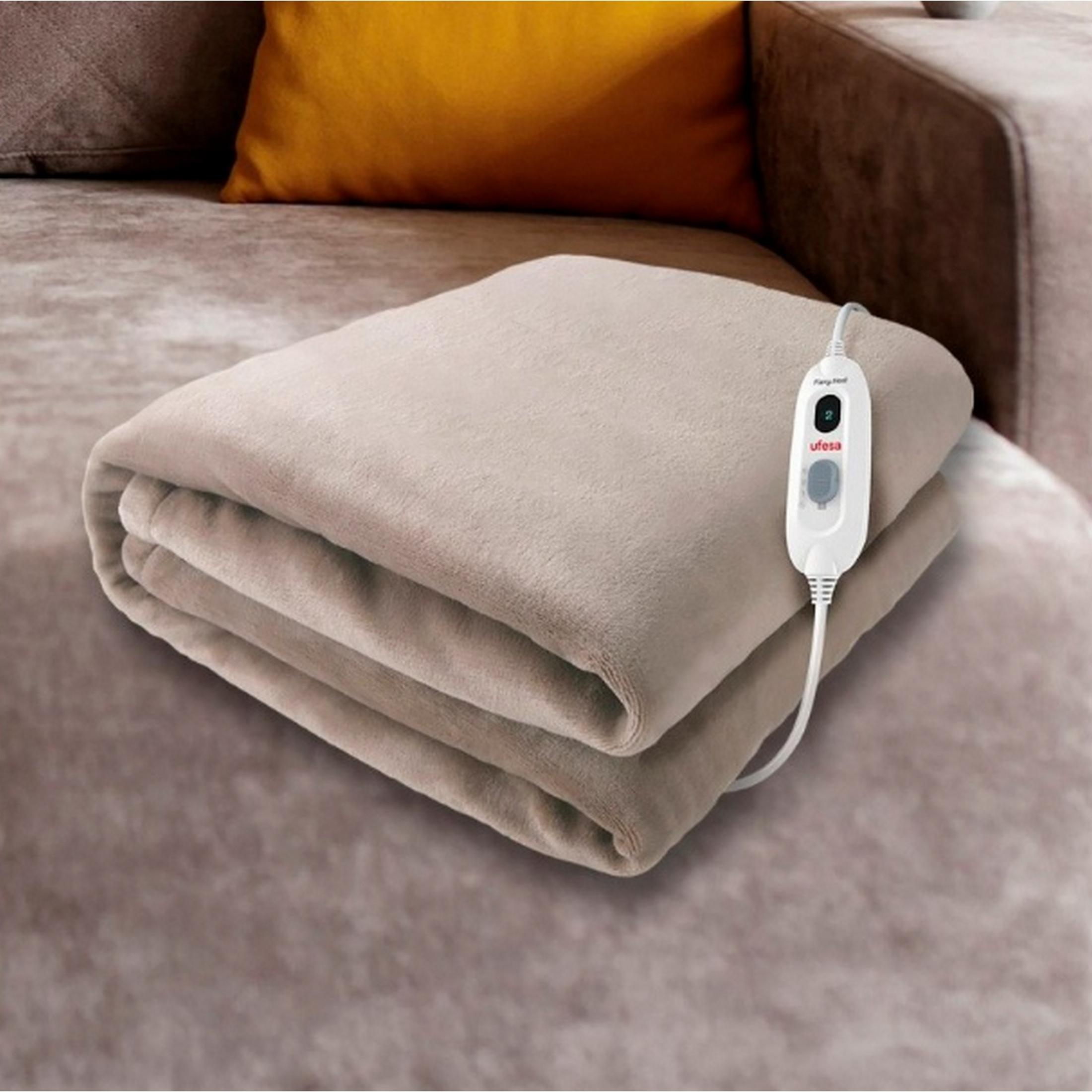 Una manta eléctrica beige doblada sobre un sofá, con un controlador.
