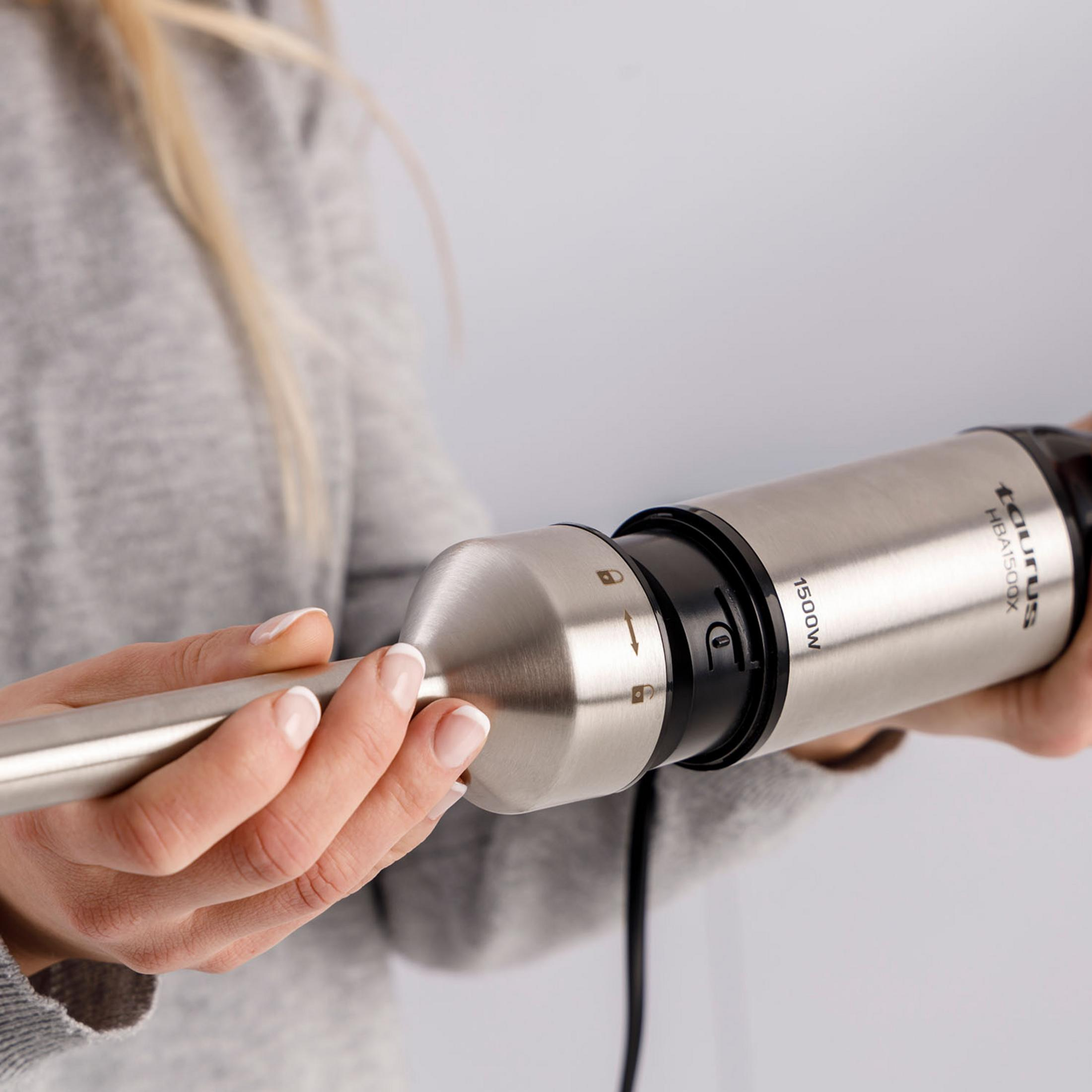 Una donna tiene un frullatore a immersione argentato con dettagli neri e 1500W.
