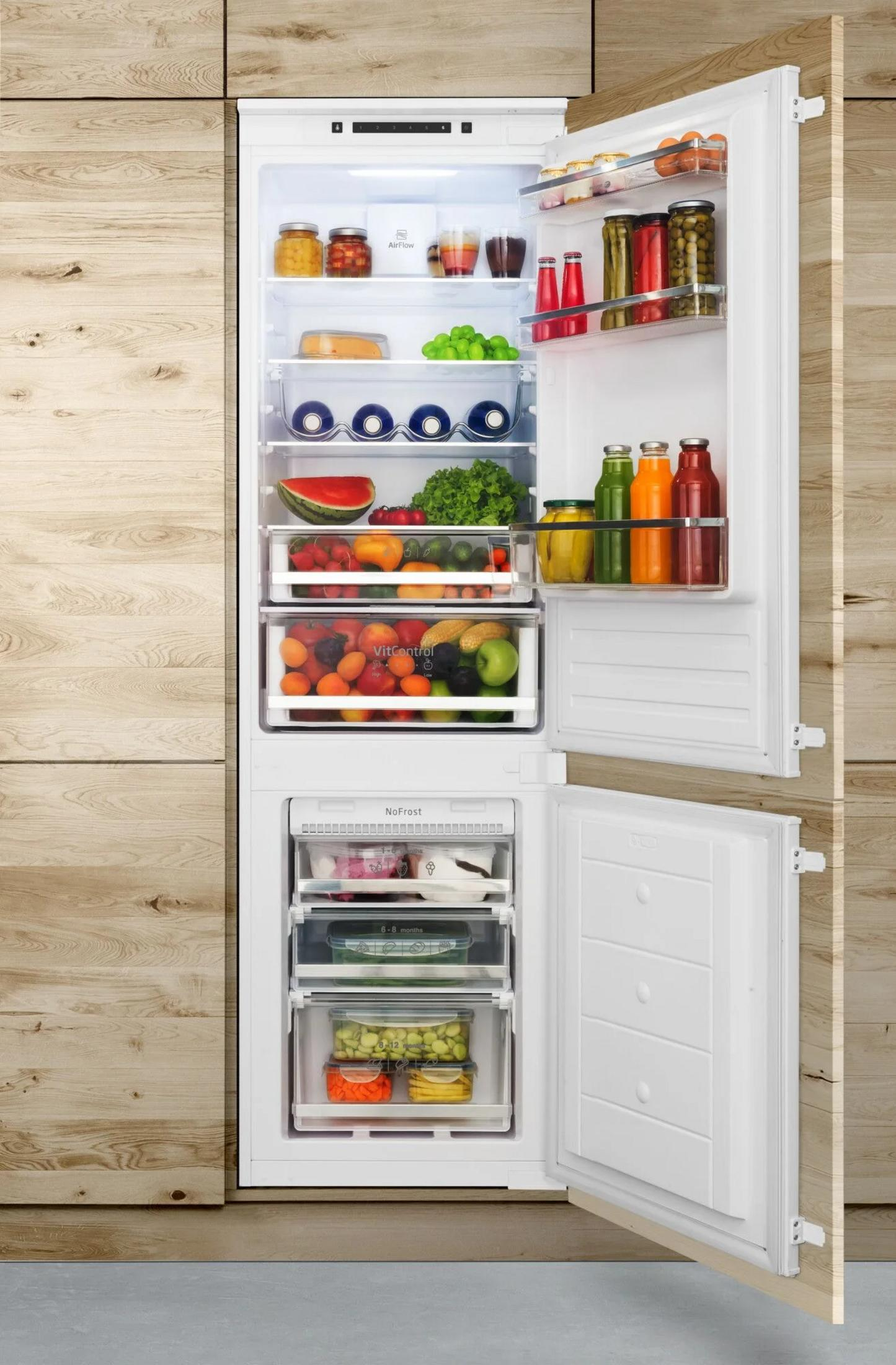 Un refrigerador abierto lleno de alimentos y cajones.