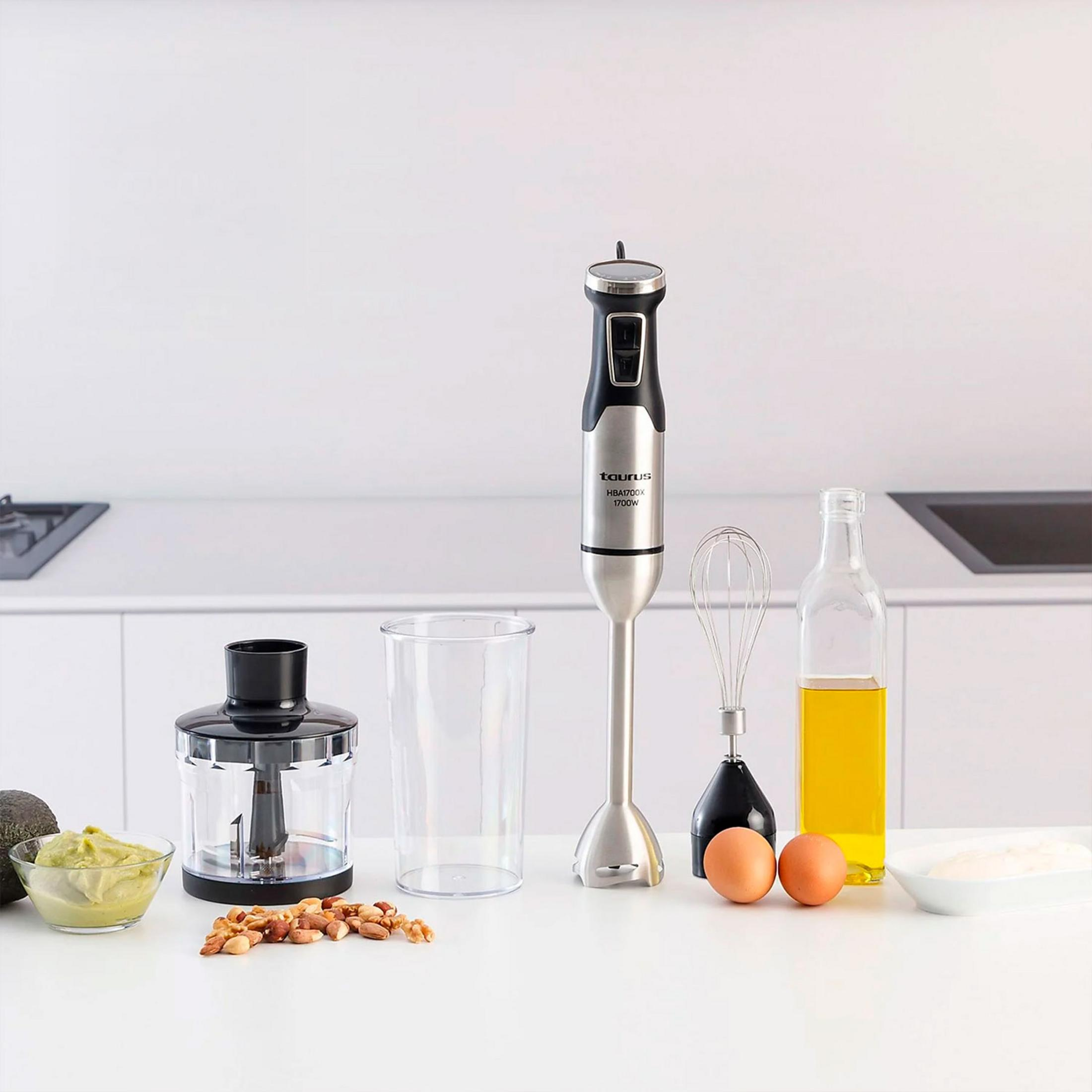 Un frullatore a immersione con accessori: tritatutto, bicchiere, frusta, uova, olio e maionese.