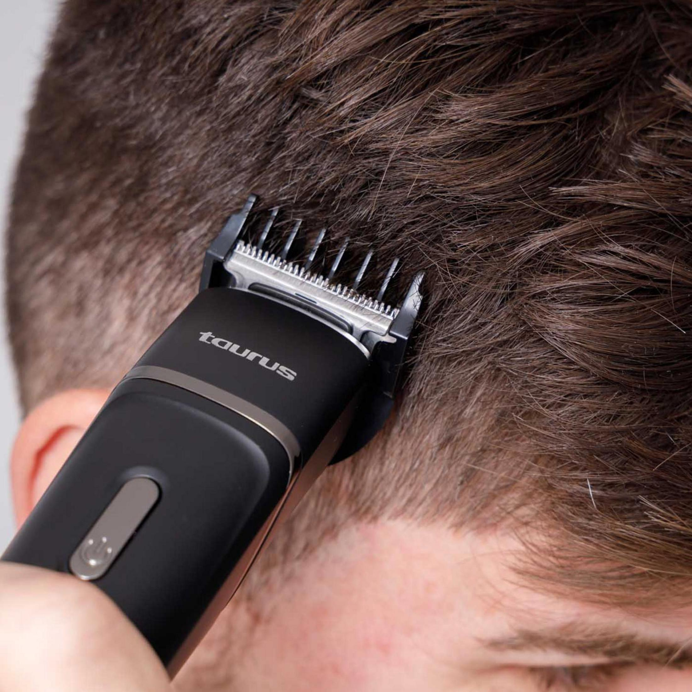 Una cortadora de pelo negra corta pelo castaño en la cabeza de un hombre.