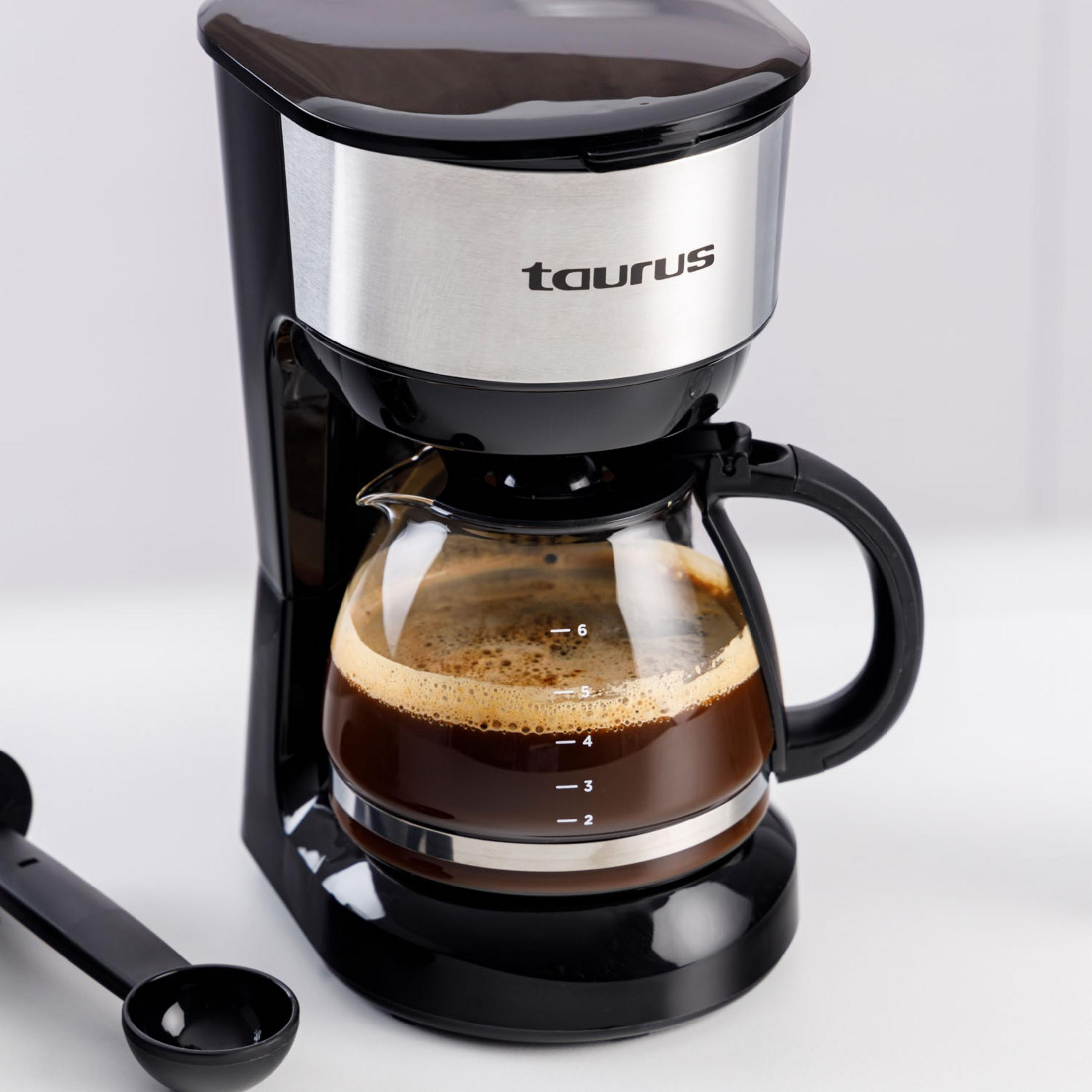 Cafetera negra con jarra de cristal llena de café. Cuchara medidora al lado.