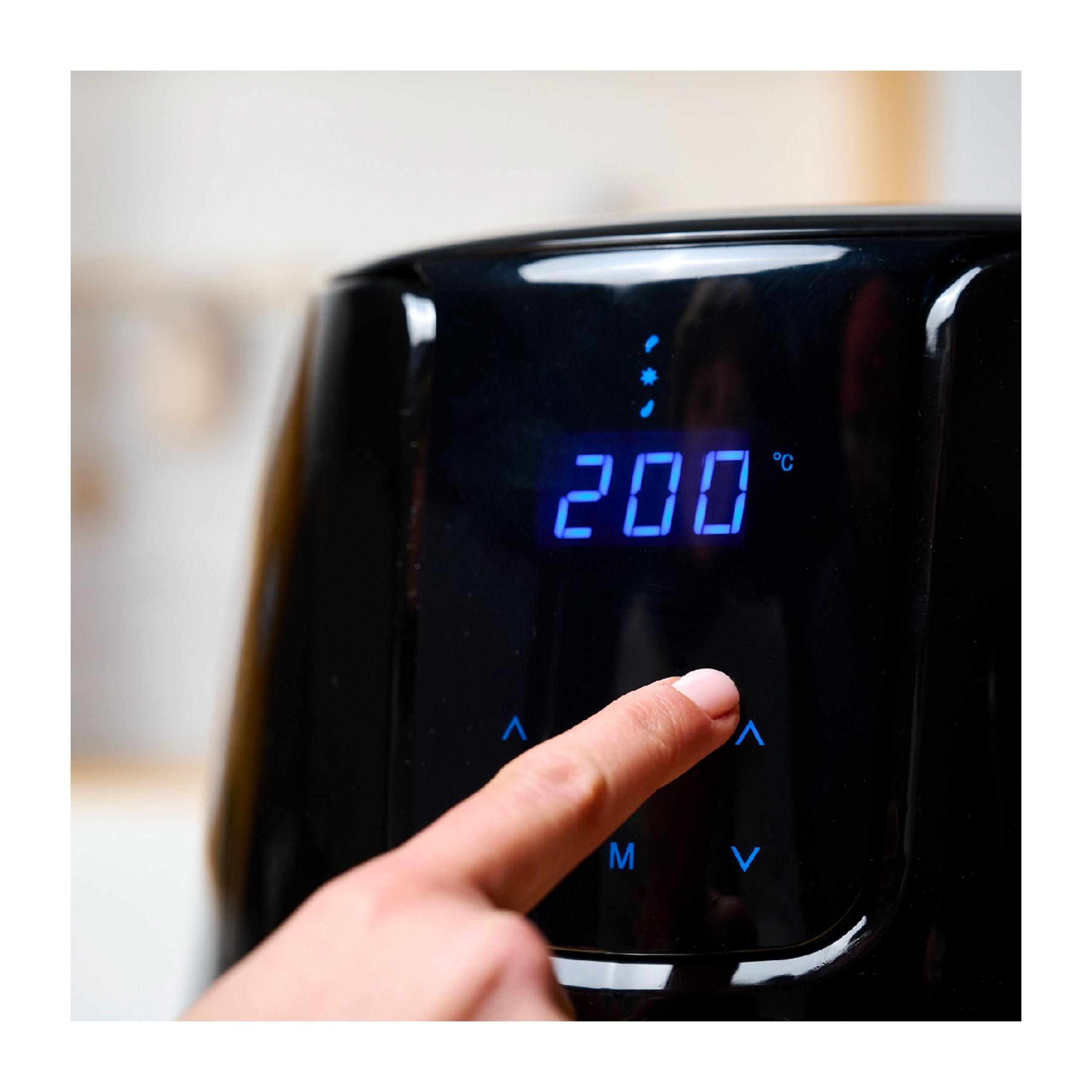 Una mano pulsa un botón en un aparato negro con pantalla digital que muestra 200°C.