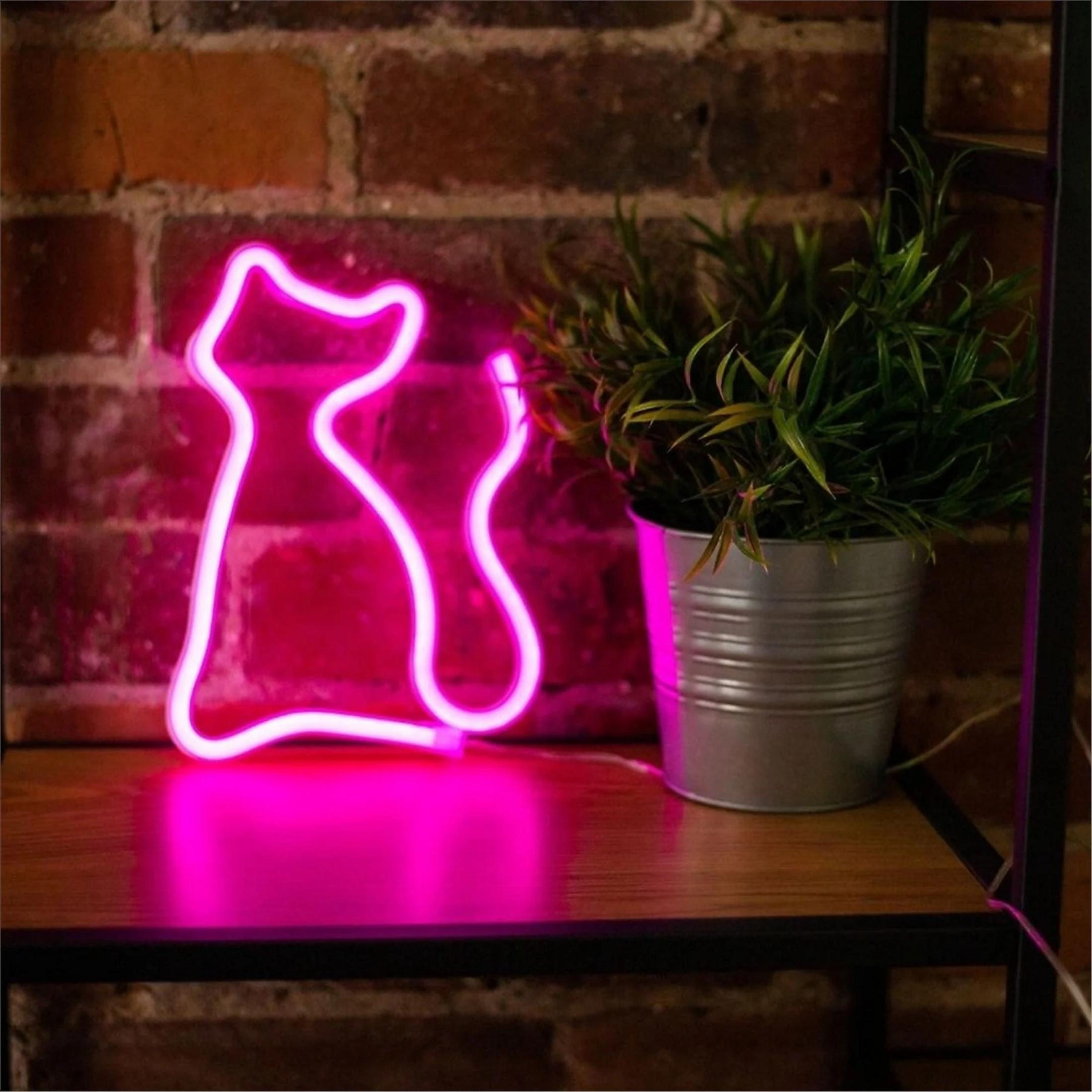 Ein pinker Neon-Katzenumriss leuchtet neben einer Topfpflanze auf einem Regal.
