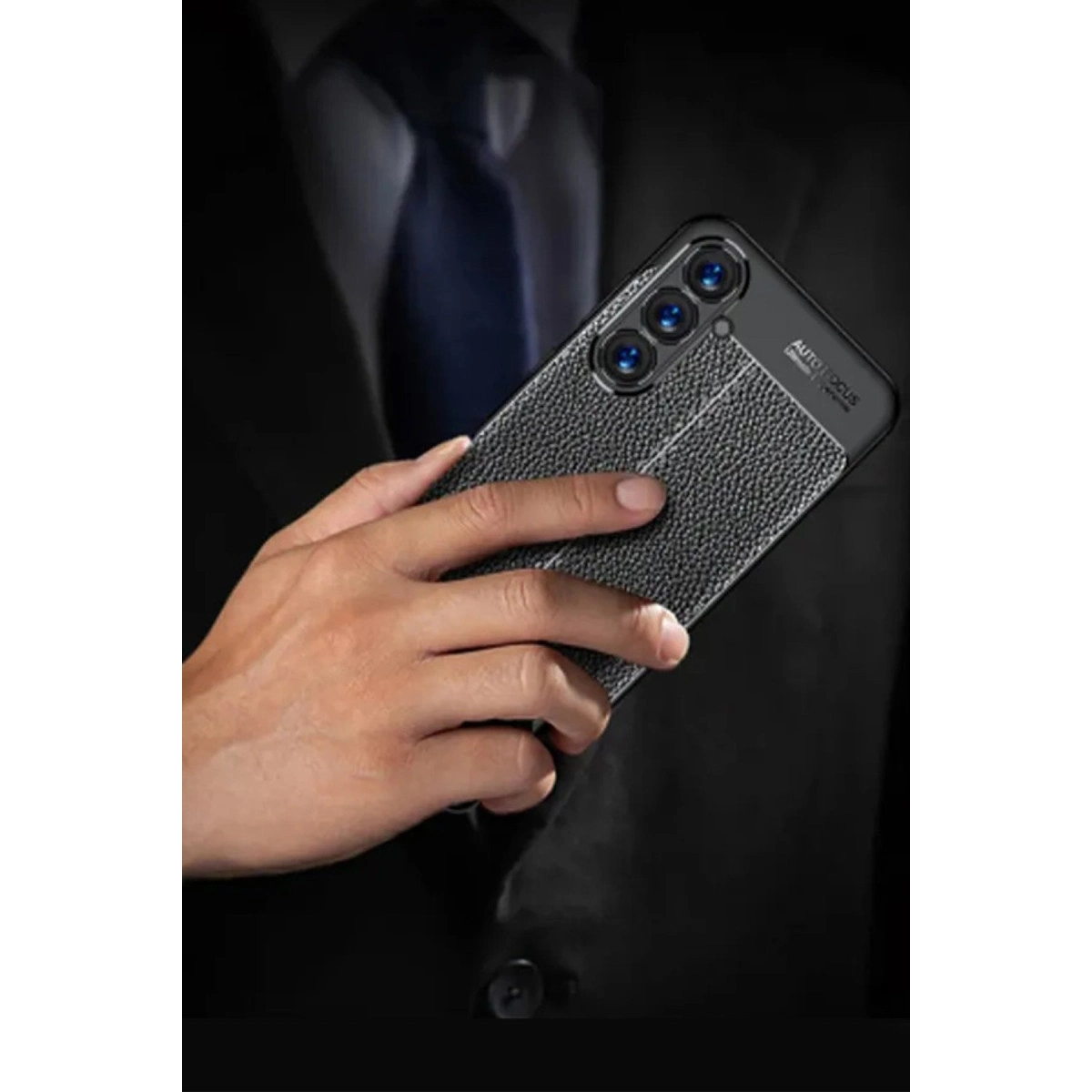 Siyah takım elbiseli adam kameralı ve dokulu arka yüzlü bir telefon tutuyor.