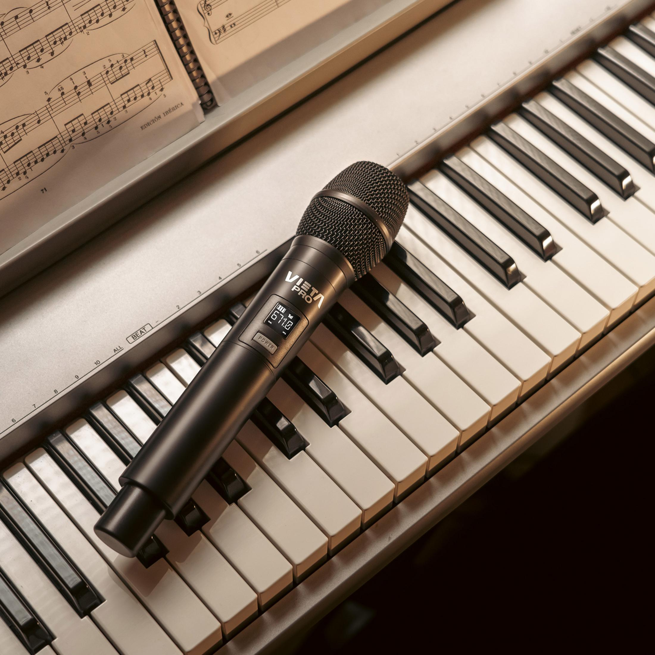 Un micrófono negro descansa sobre un teclado de piano junto a partituras.