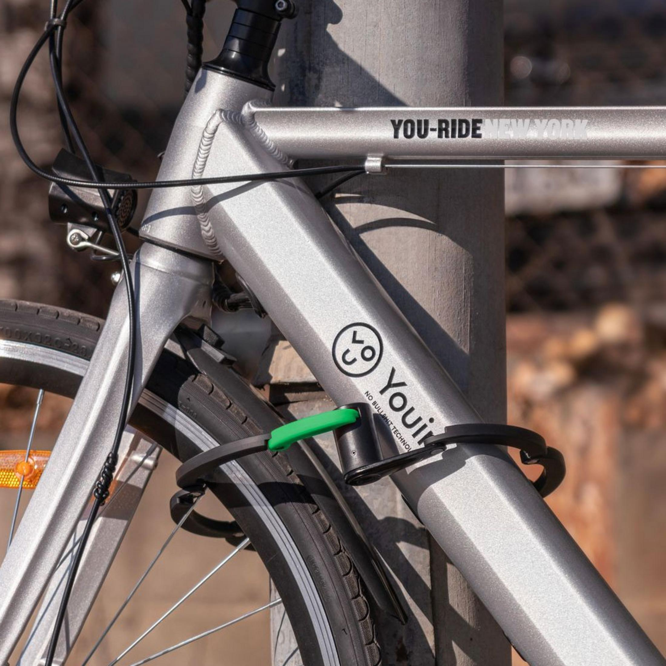 Una bicicleta plateada con un candado negro atado a un poste. Dice YOU-RIDE NEW YORK.