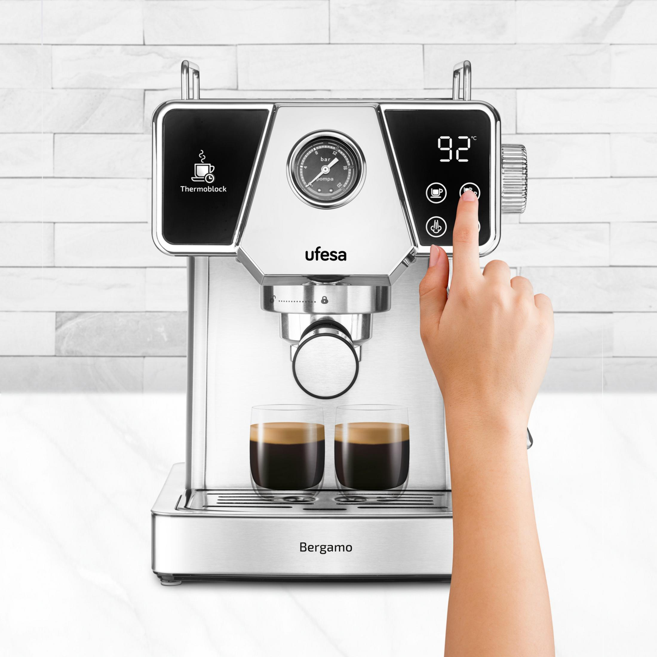 Un dedo presiona una máquina de espresso con dos tazas de espresso.