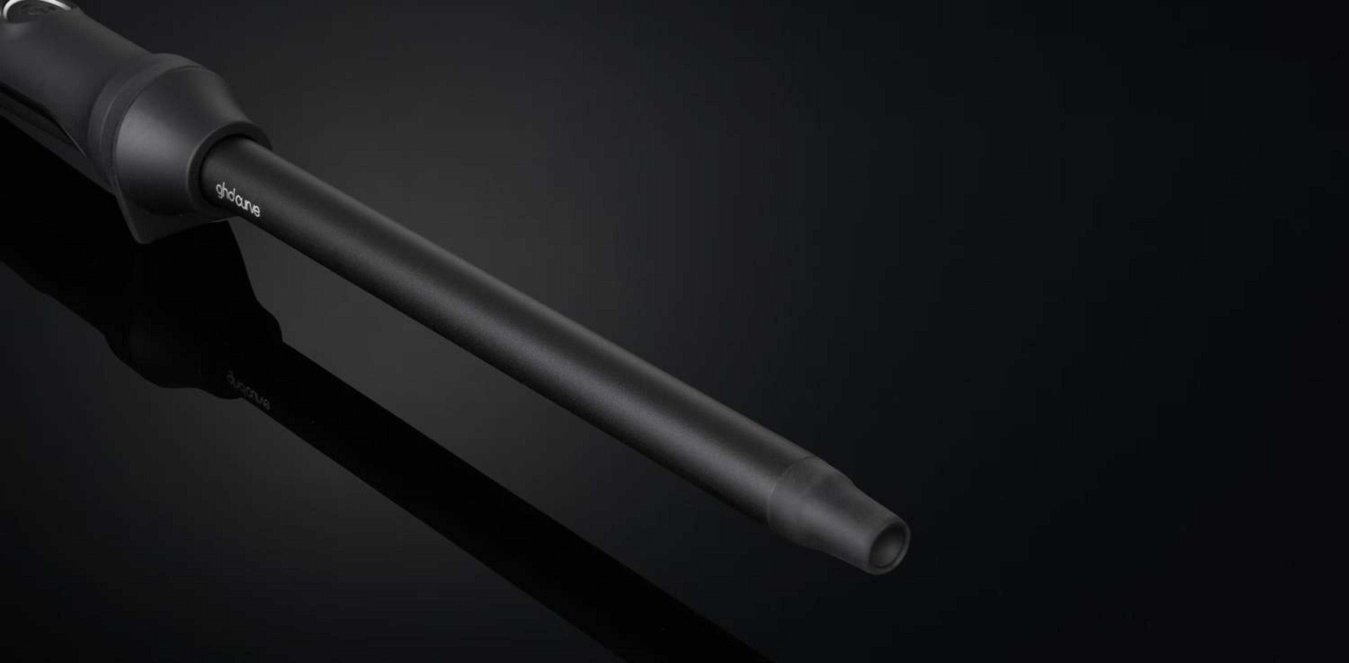 Un rizador de pelo negro con mango elegante y barril cilíndrico sobre fondo oscuro.