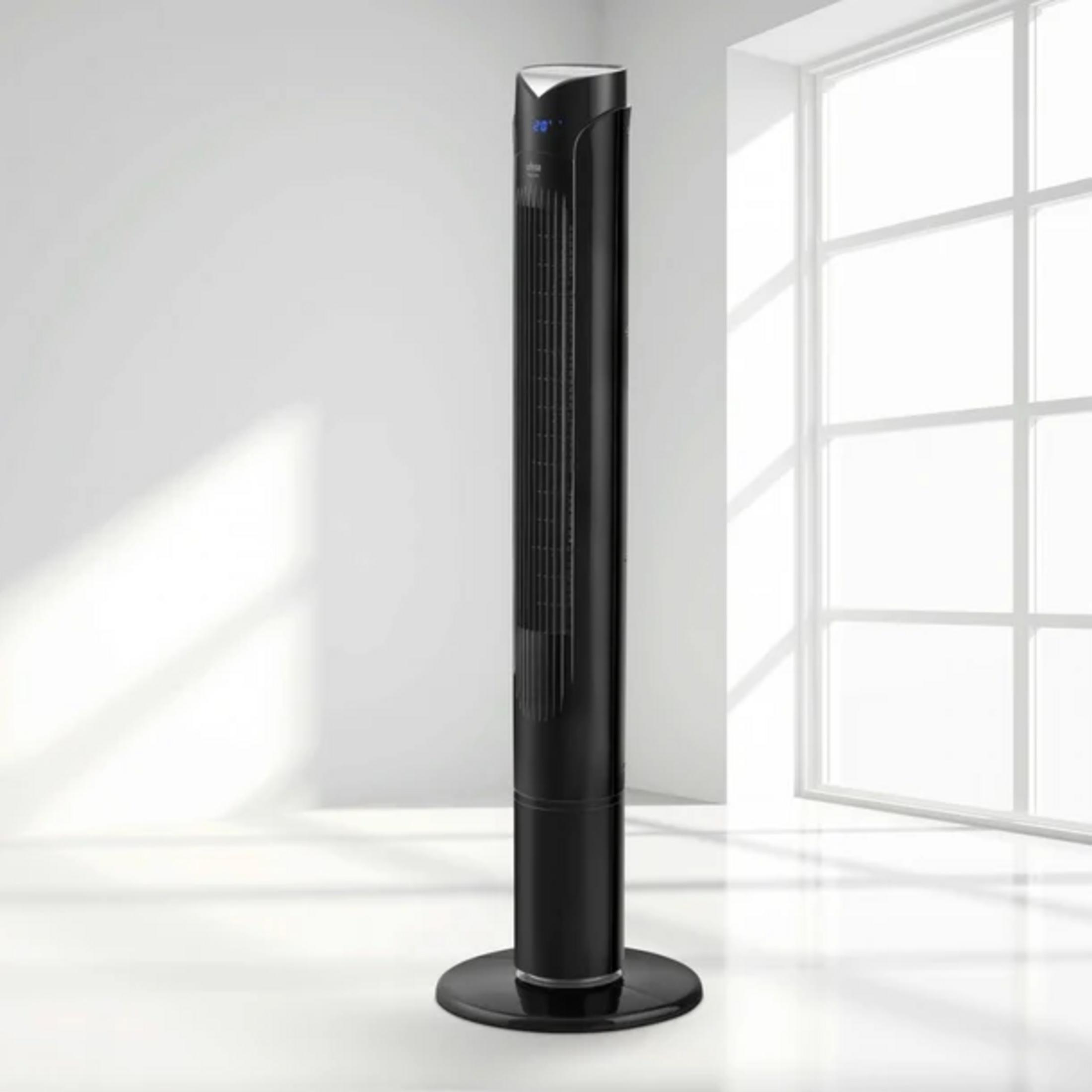 Un ventilador de torre negro y elegante se alza sobre una base redonda junto a una ventana.