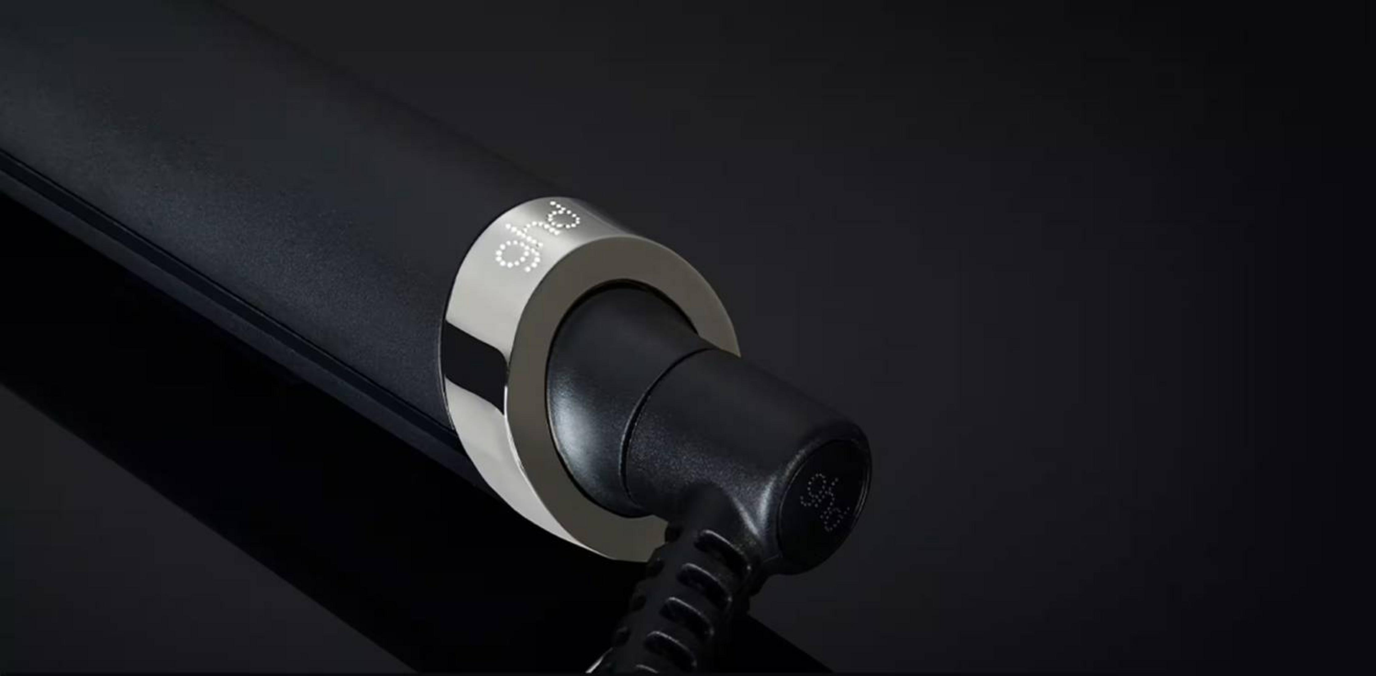 Primer plano del mango de secador de pelo negro con anillo plateado y logo 'ghd' iluminado.
