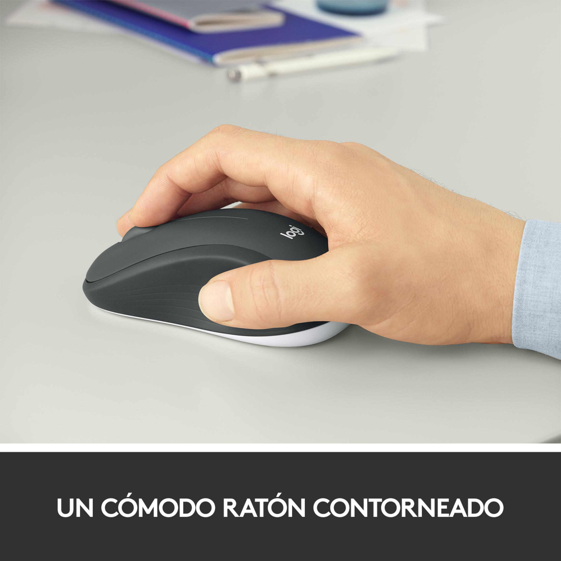 Una mano tiene un mouse Logitech grigio su una scrivania grigio chiaro. Quaderni sullo sfondo.