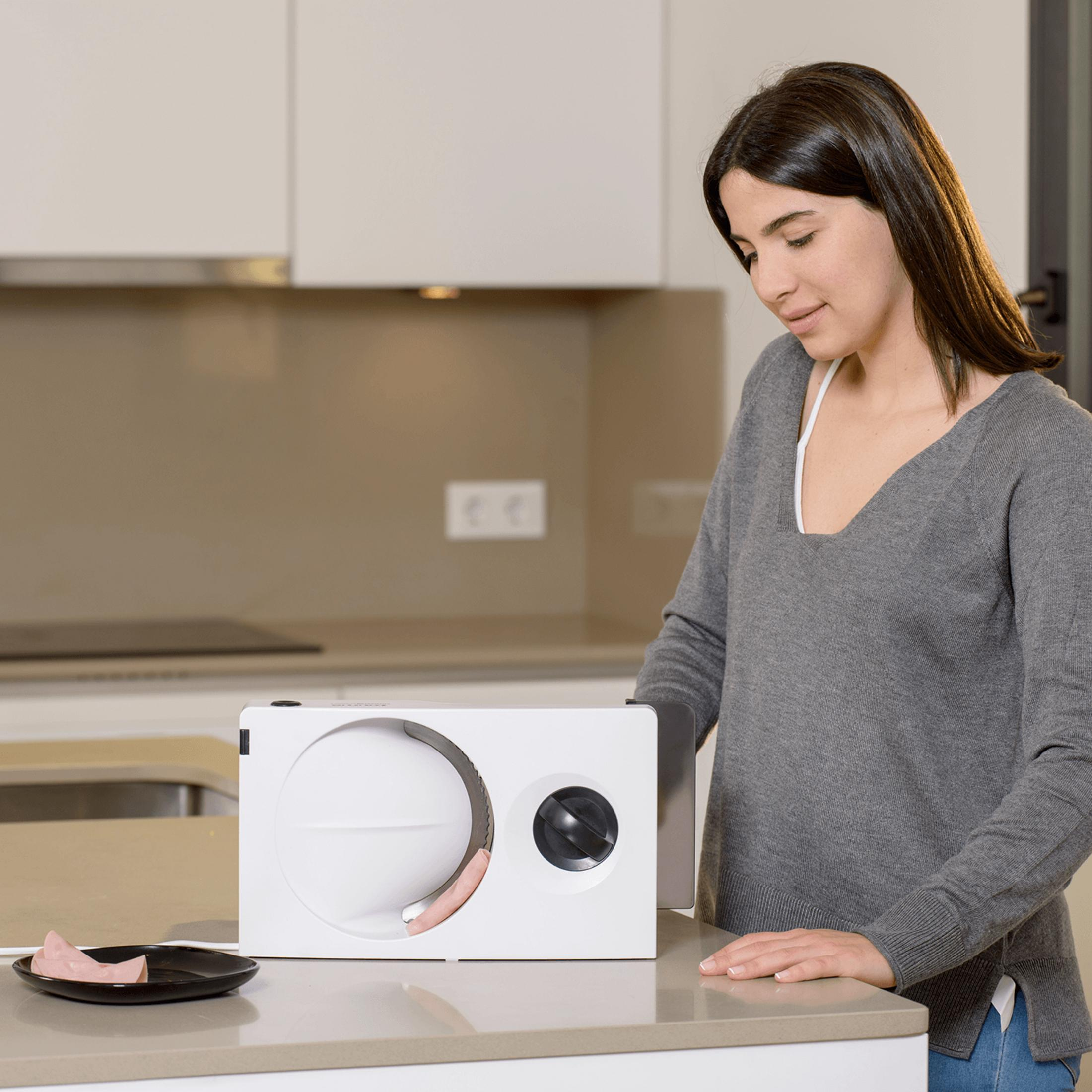 Una donna affetta prosciutto in cucina con un'affettatrice elettrica.
