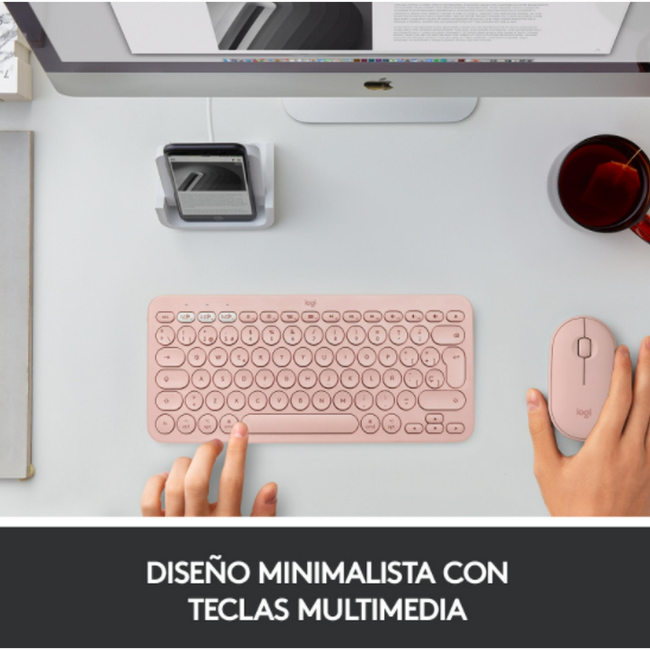 Un teclado y ratón rosas están sobre un escritorio junto a un iMac y una taza de té.