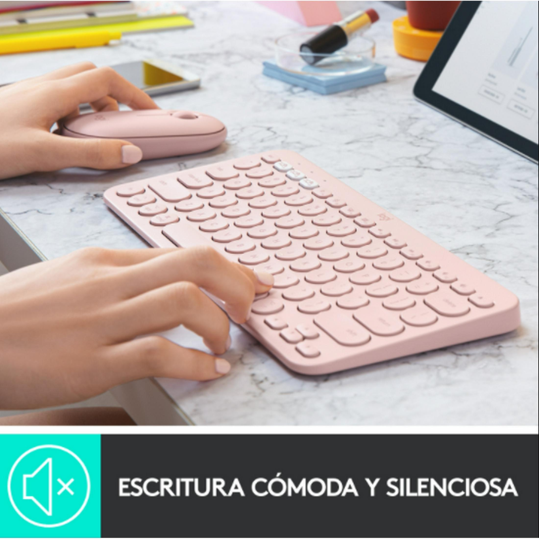 Una mano usa un teclado y ratón rosas en un escritorio. Suministros de oficina al fondo.