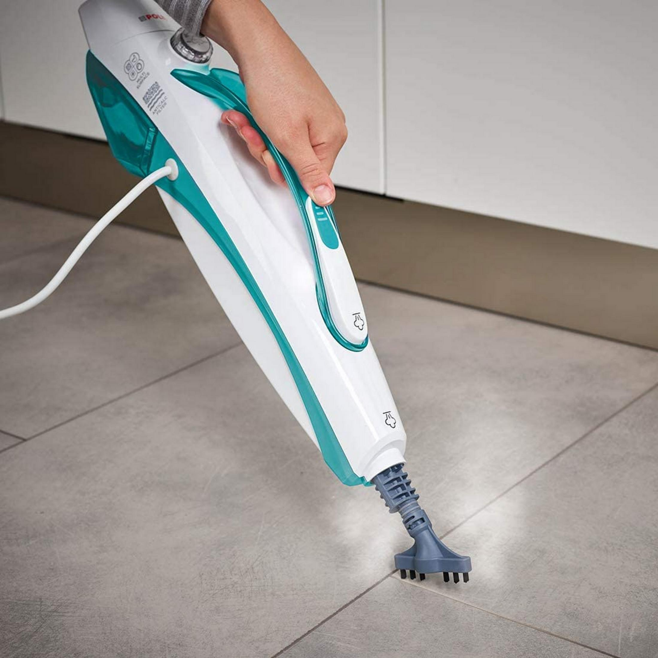 A hand holds a white and teal steam cleaner over grey tiles.
