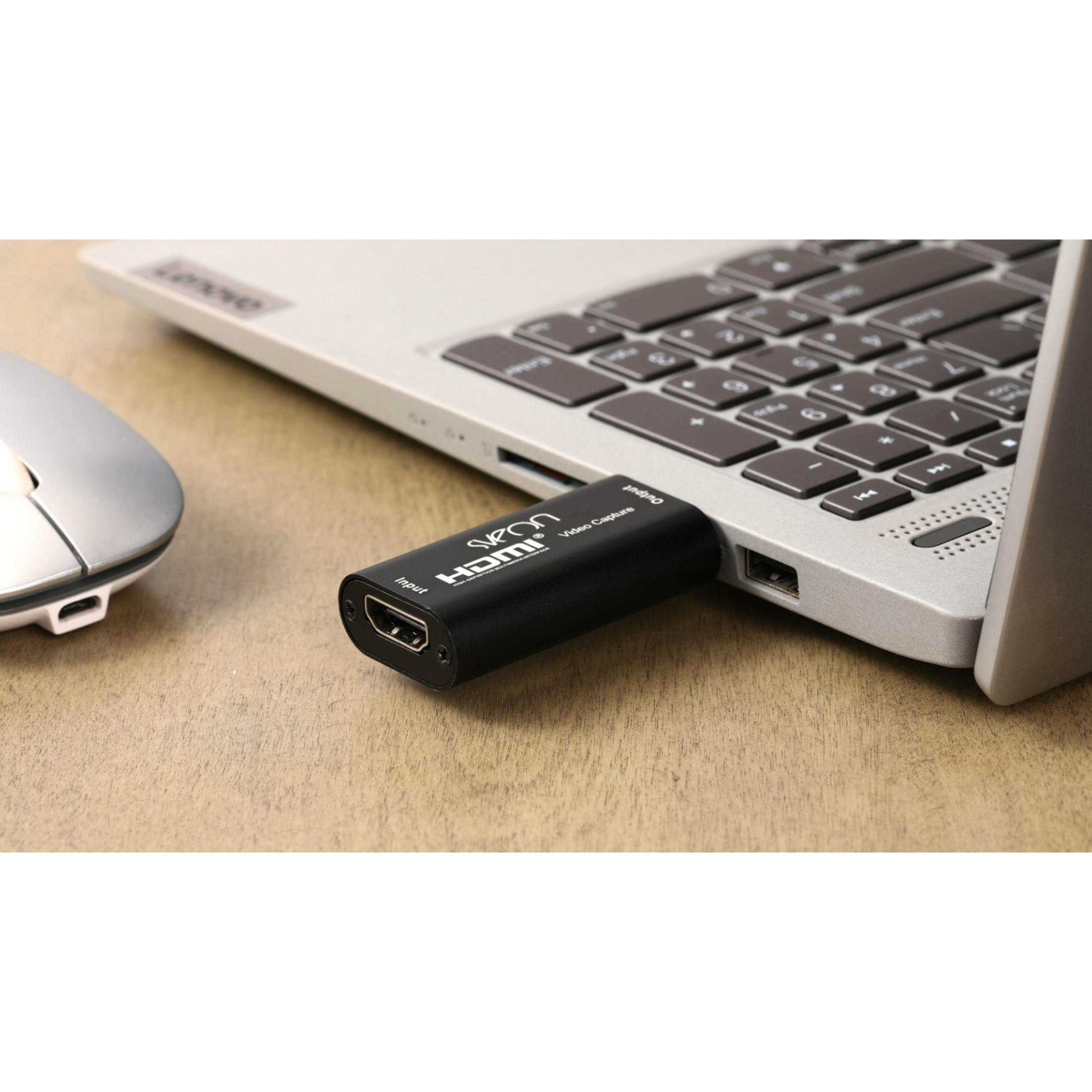 Un dongle de captura de video HDMI negro está enchufado a un portátil, con un ratón cerca.