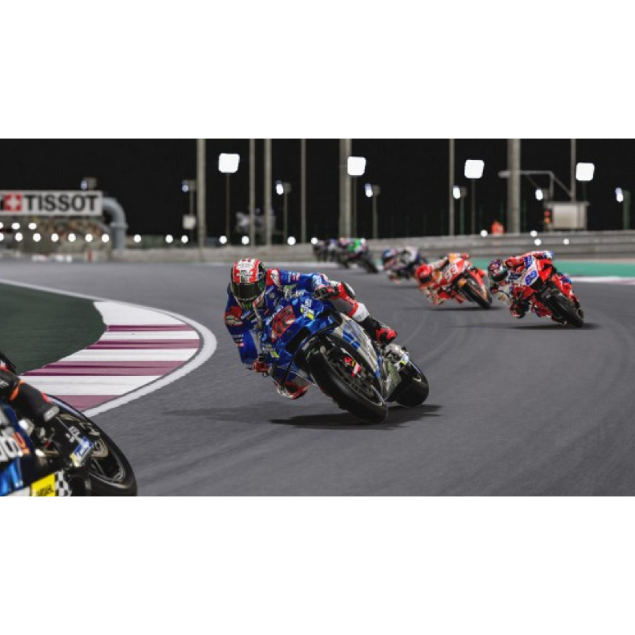 Motociclisti in tenuta blu e rossa corrono su una pista di notte, con luci e tribuna sullo sfondo.
