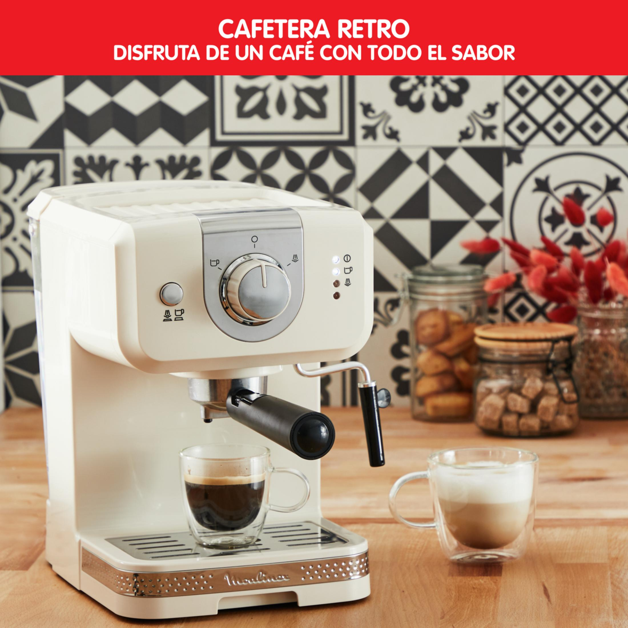 Una cafetera retro color crema con dos tazas de café sobre una mesa de madera.