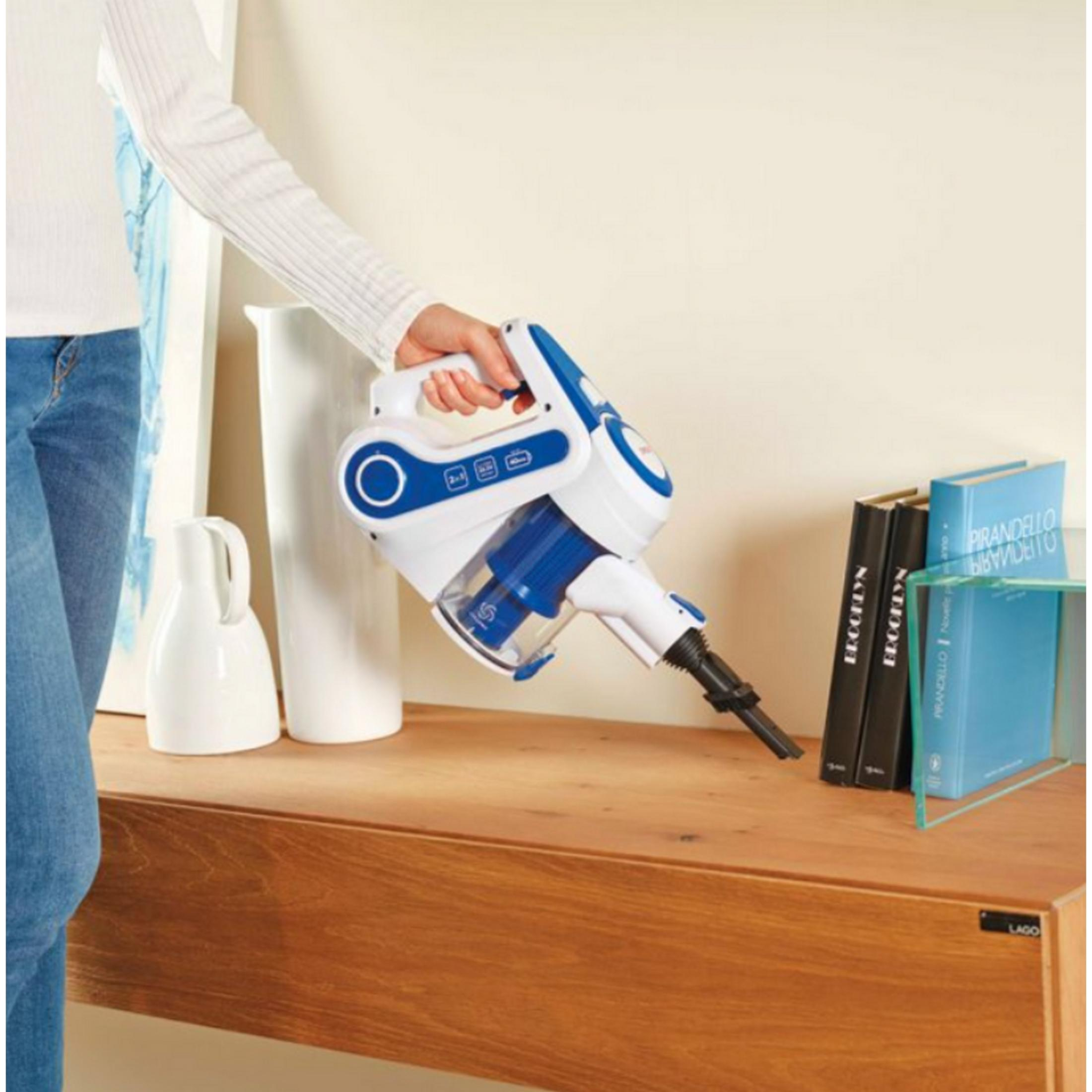 Una mano tiene un aspirapolvere bianco e blu su un tavolo di legno con libri.