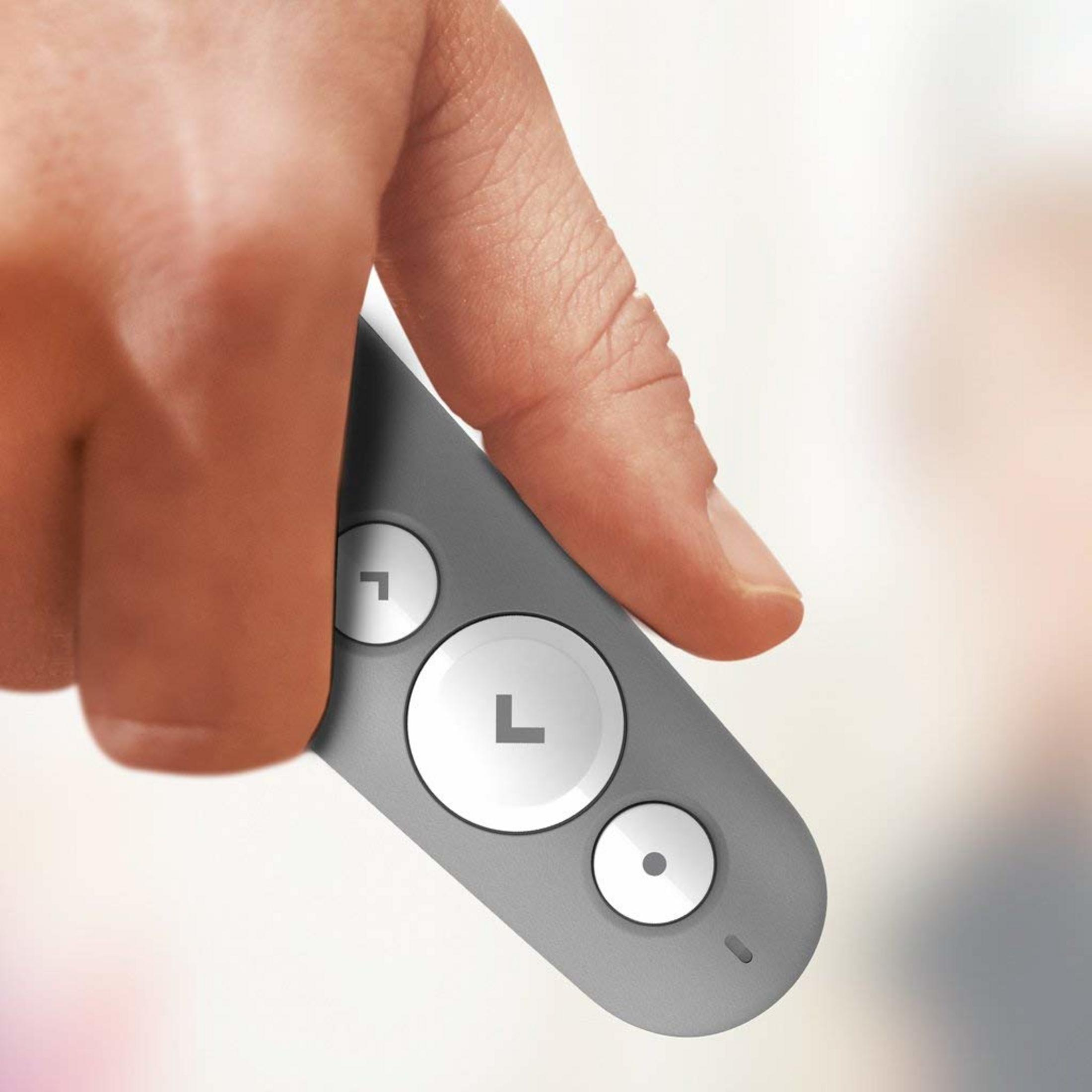 El pulgar y el índice de una persona sostienen un control remoto gris con tres botones redondos.