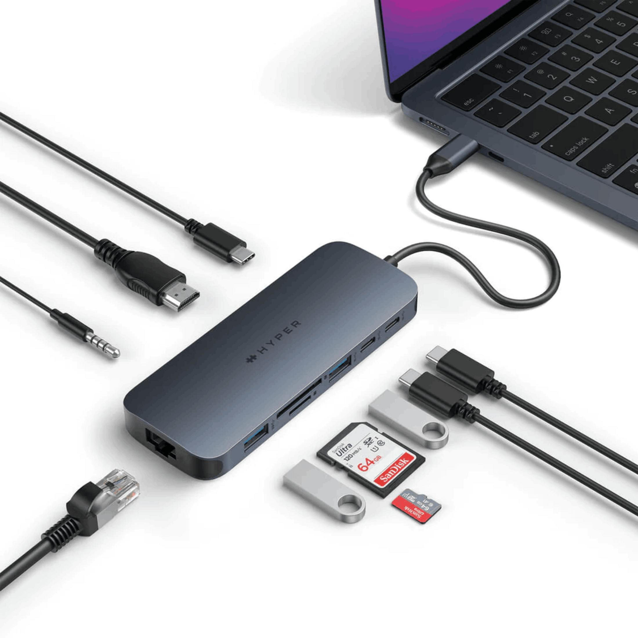 Un hub USB-C scuro è collegato a un laptop, con schede SD e cavi accanto.