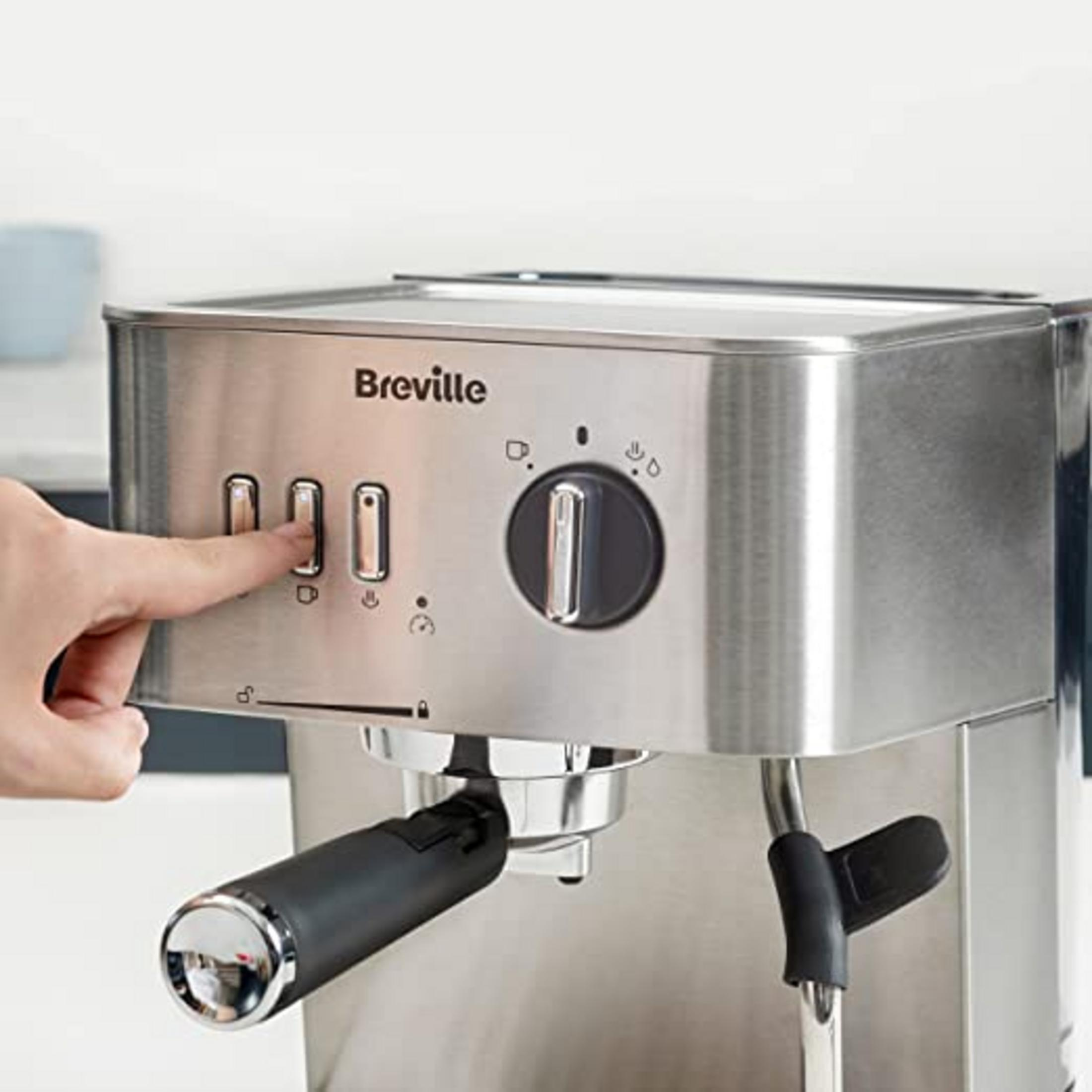 Una mano presiona un botón en una cafetera Breville plateada. Primer plano.