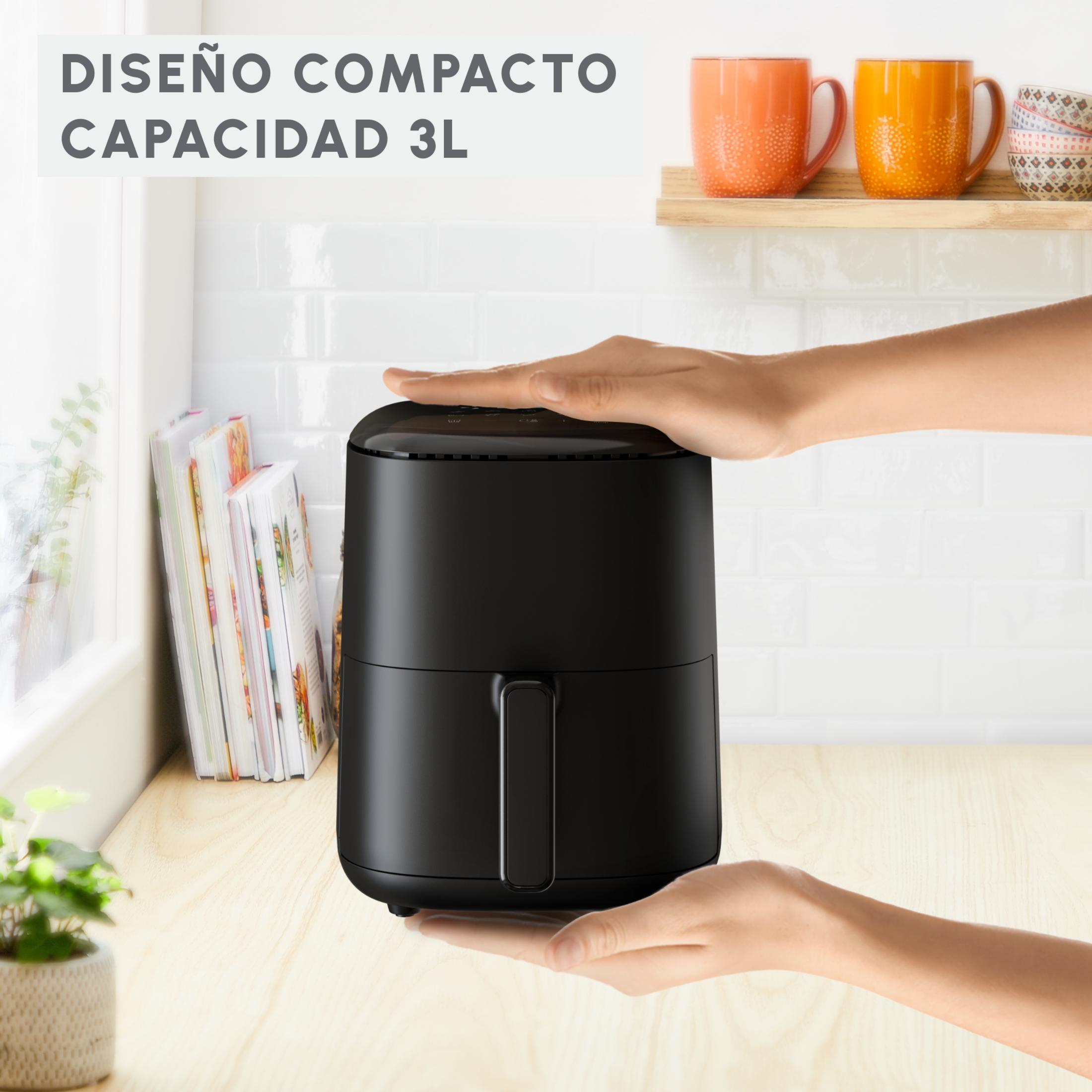 Friggitrice ad aria nera con mani, libri di cucina e tazze sullo sfondo.
