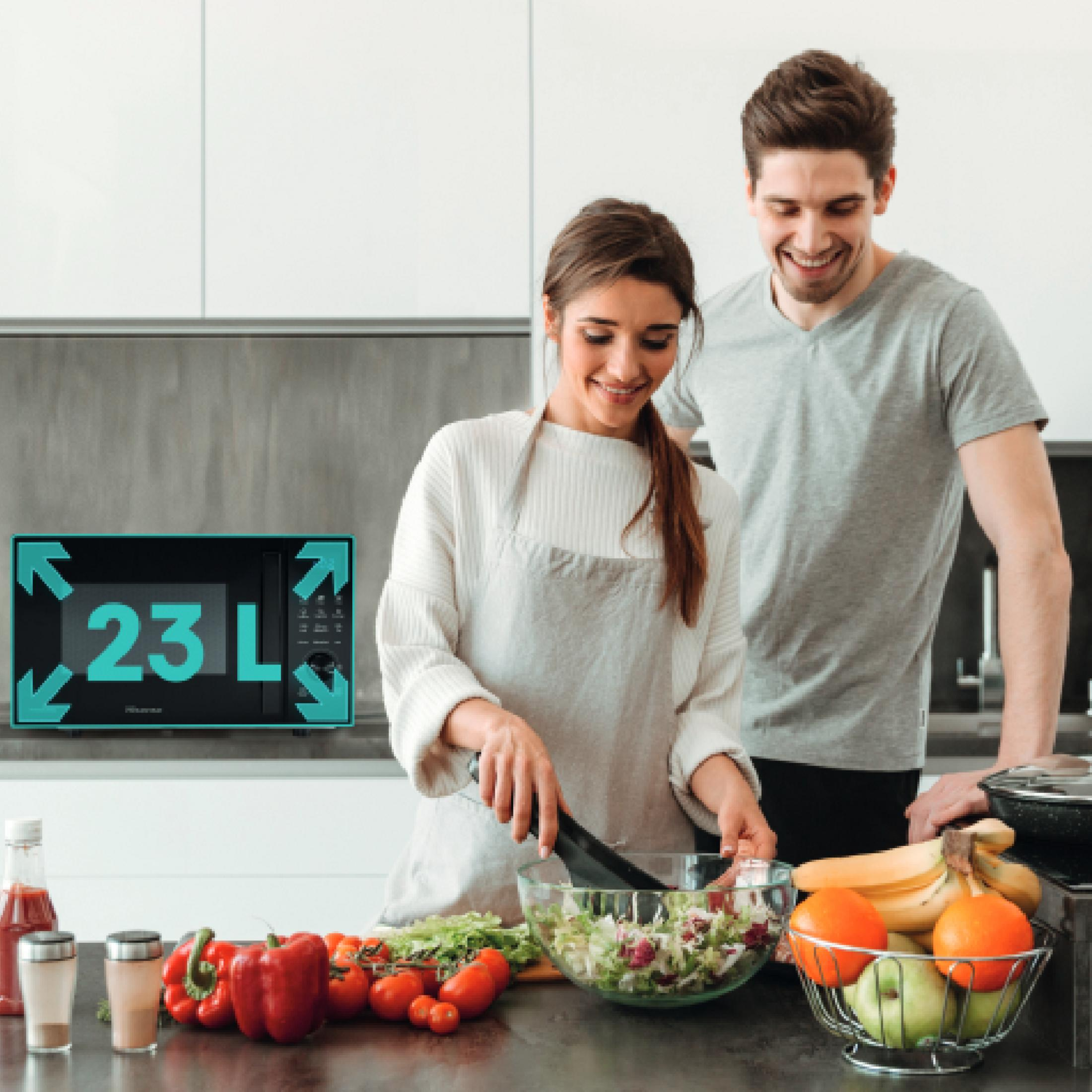 Una pareja prepara una ensalada en una cocina moderna. Un microondas está al fondo.