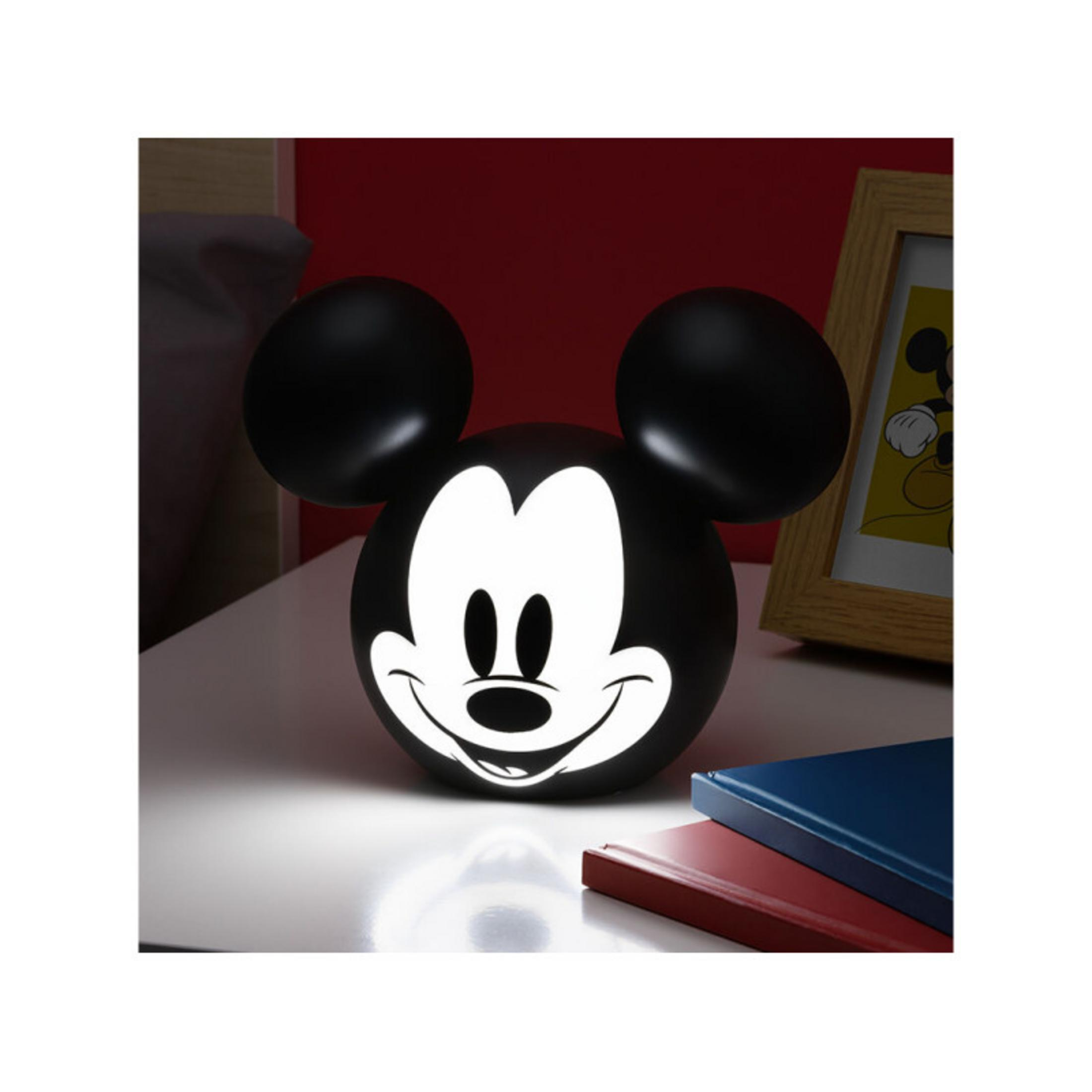 Una lámpara de Mickey Mouse en una mesita de noche con libros.