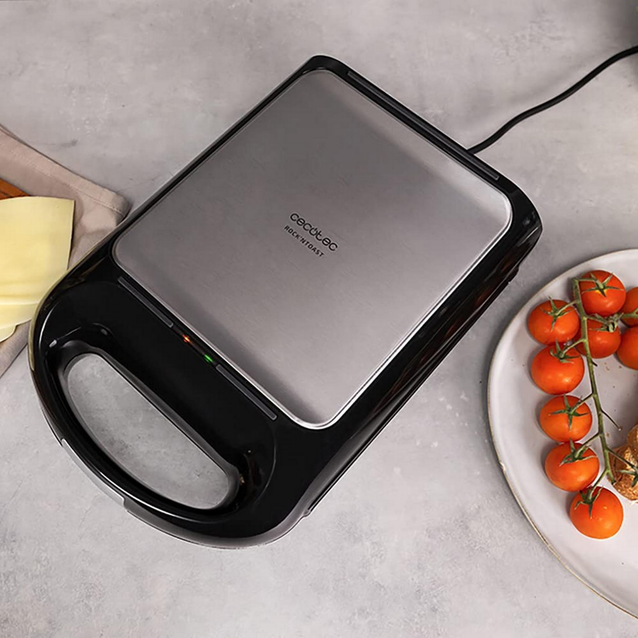A black and silver contact grill sits on a gray counter next to tomatoes.