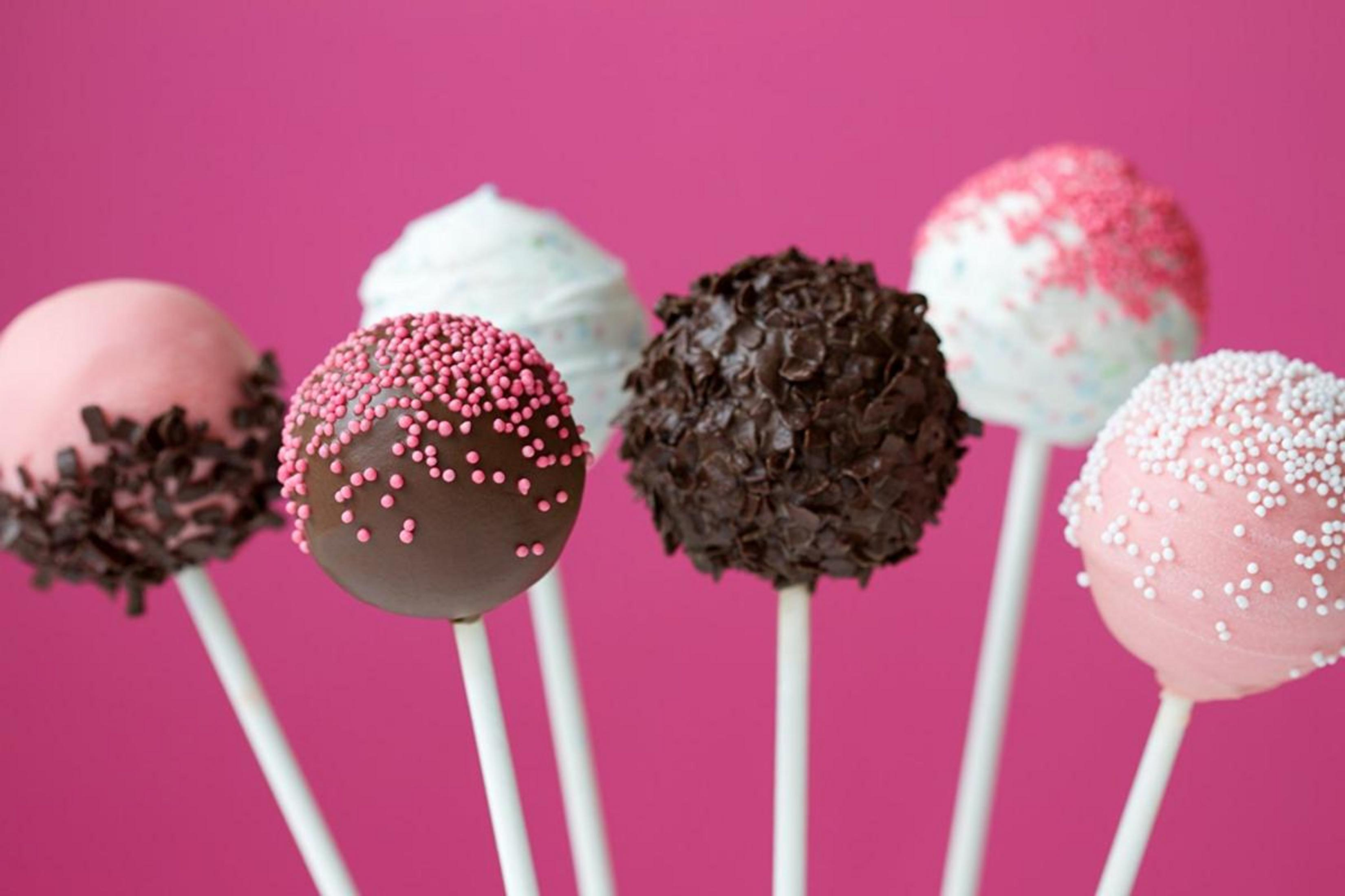 Seis cake pops en palitos, decorados con virutas de chocolate y perlas rosas/blancas.