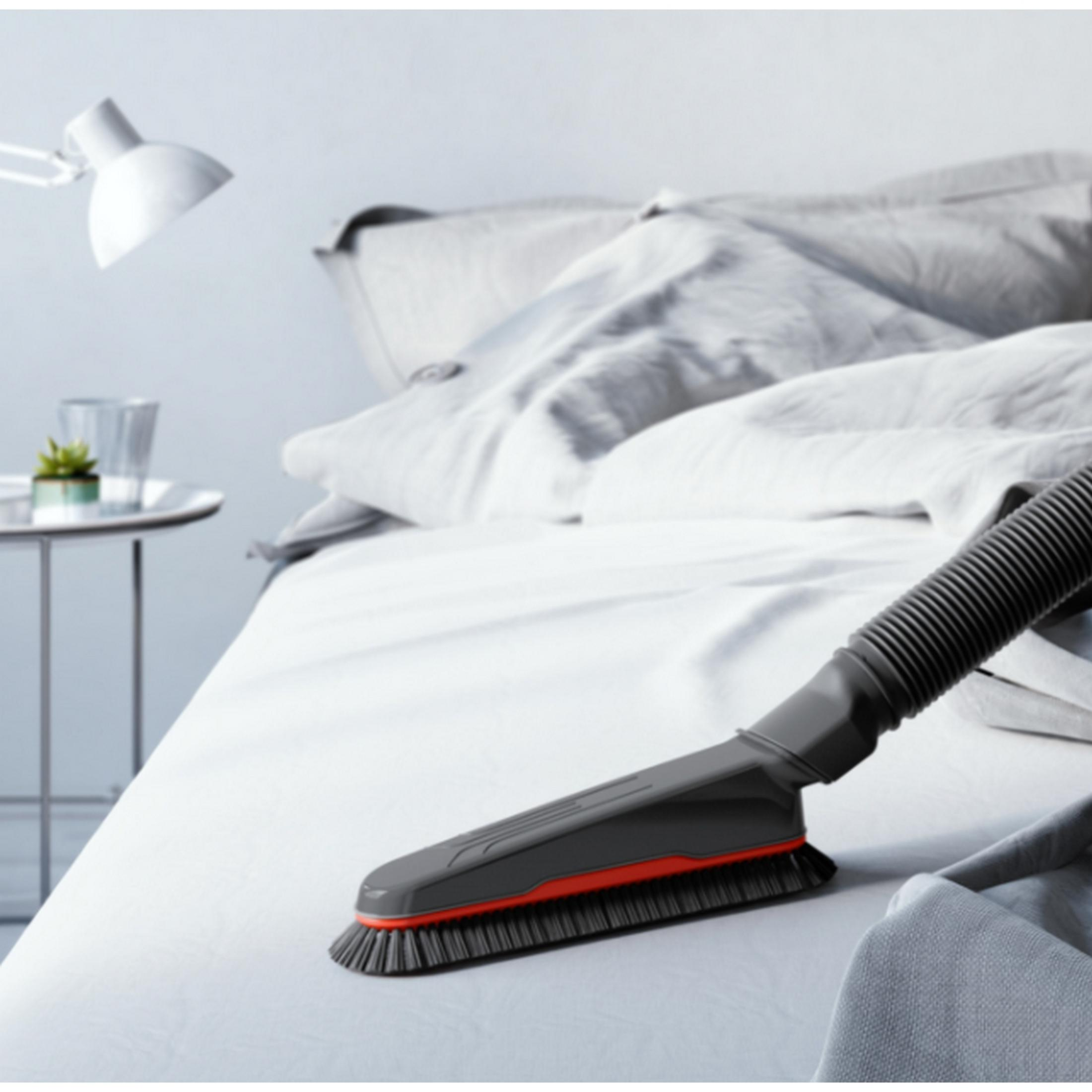 Un accessorio per aspirapolvere con spazzola su un letto bianco.