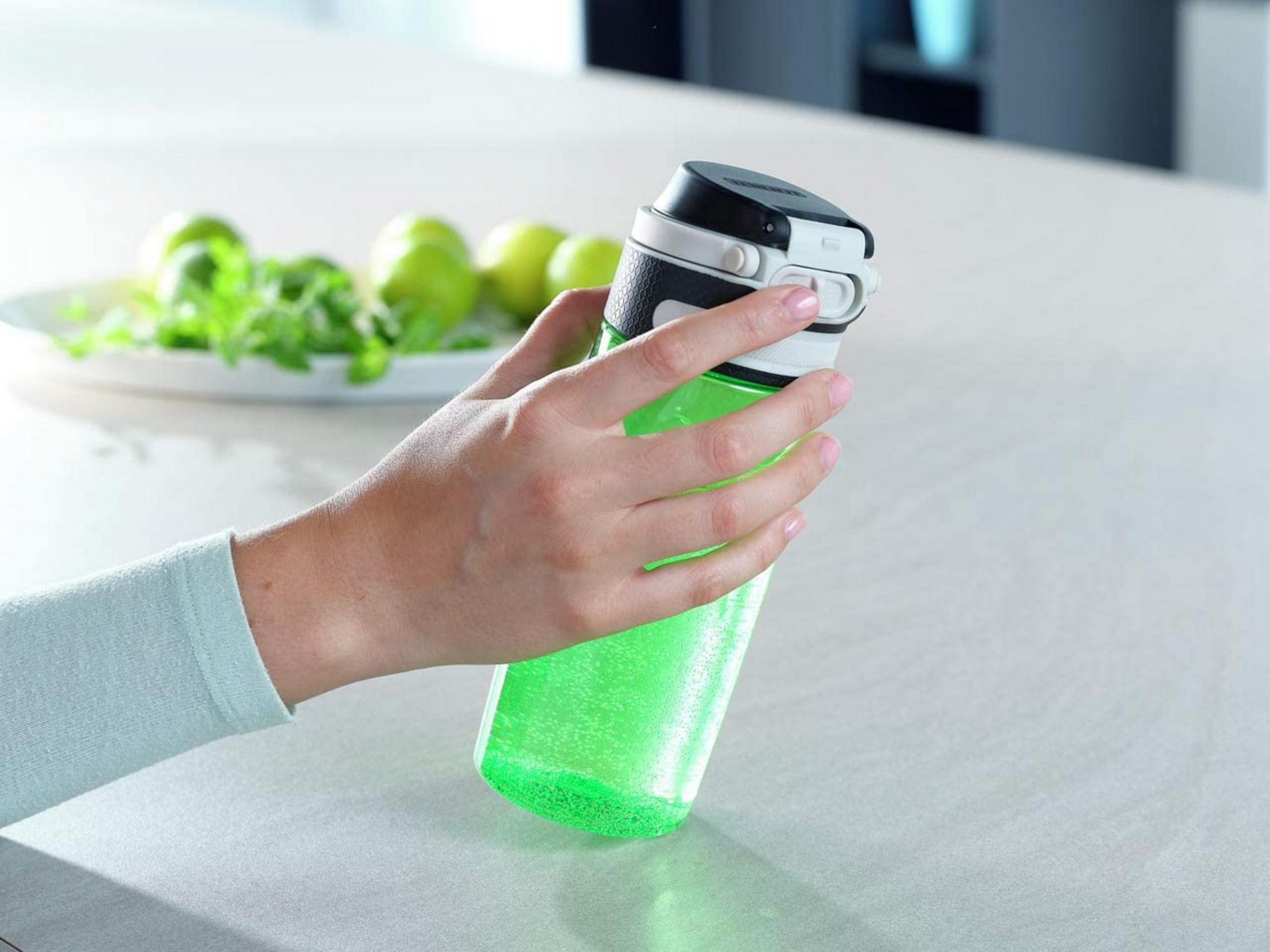 Una mano sostiene una botella verde transparente con líquido burbujeante.