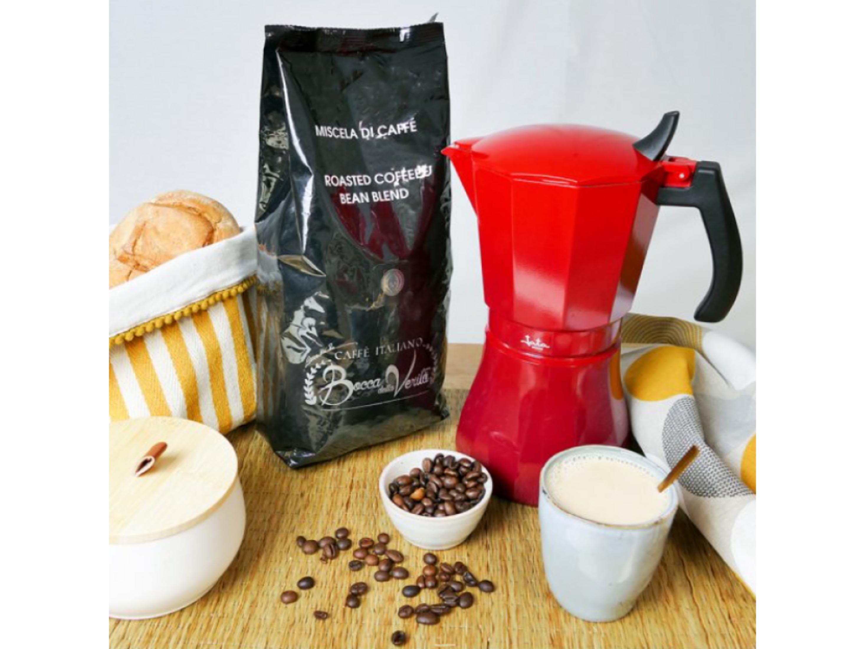 Una caffettiera moka rossa, chicchi di caffè, pane e una tazza di caffè.
