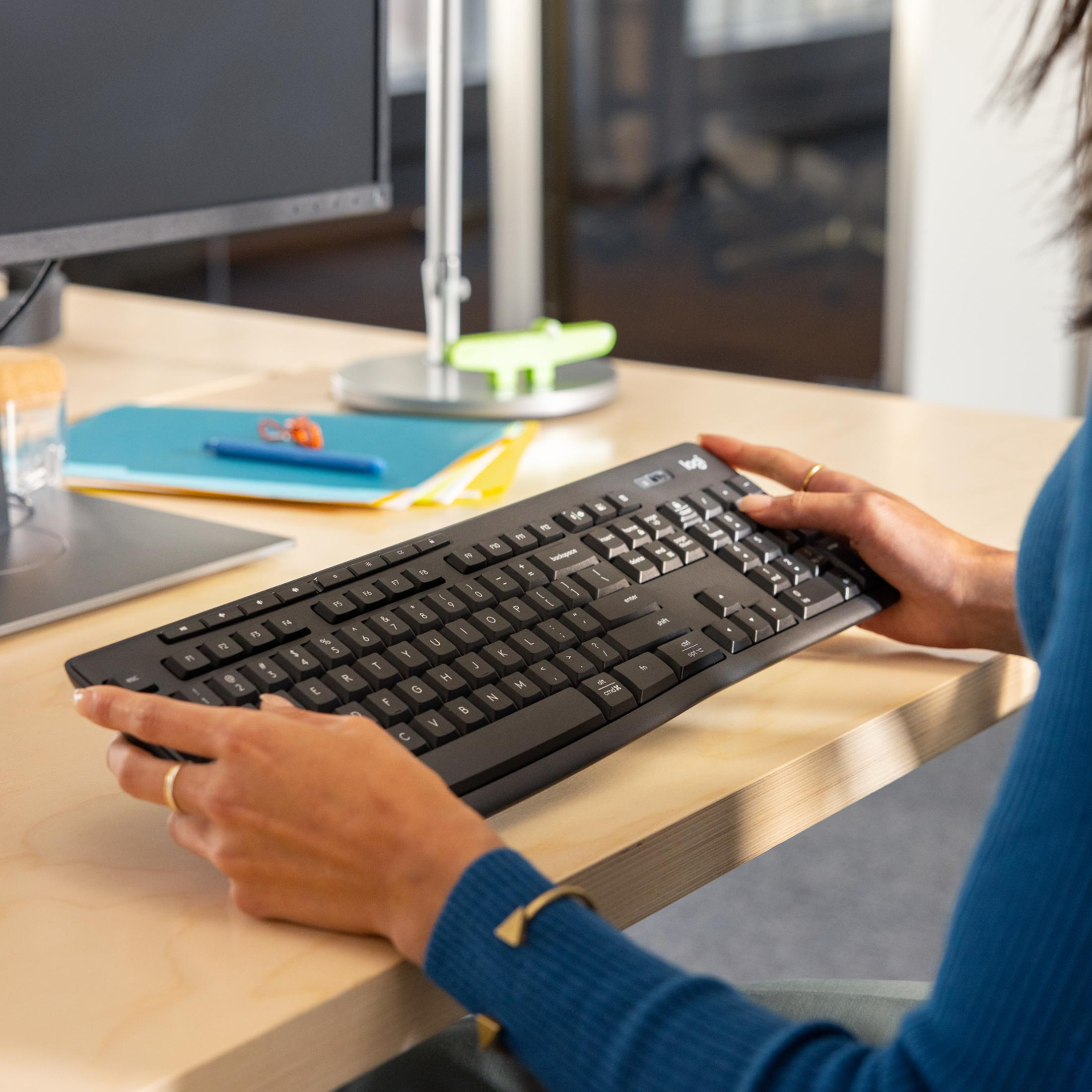 Una persona digita su una tastiera Logitech nera a una scrivania.